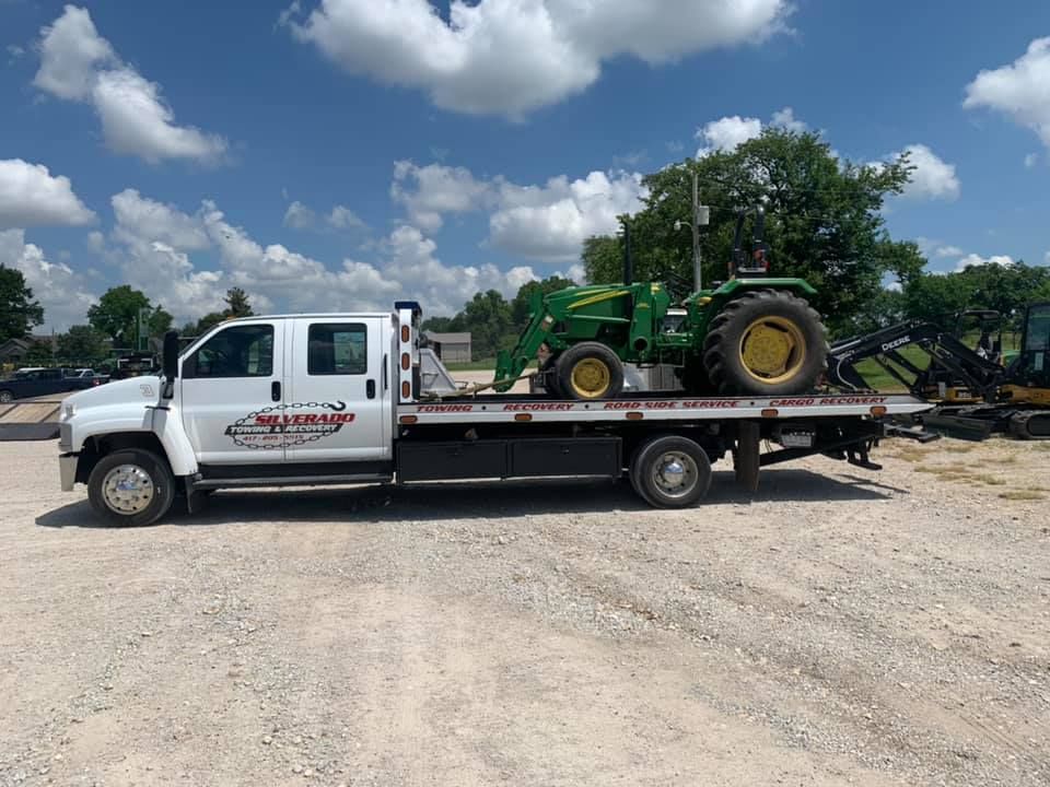 A tow truck is carrying a green john deere tractor.
