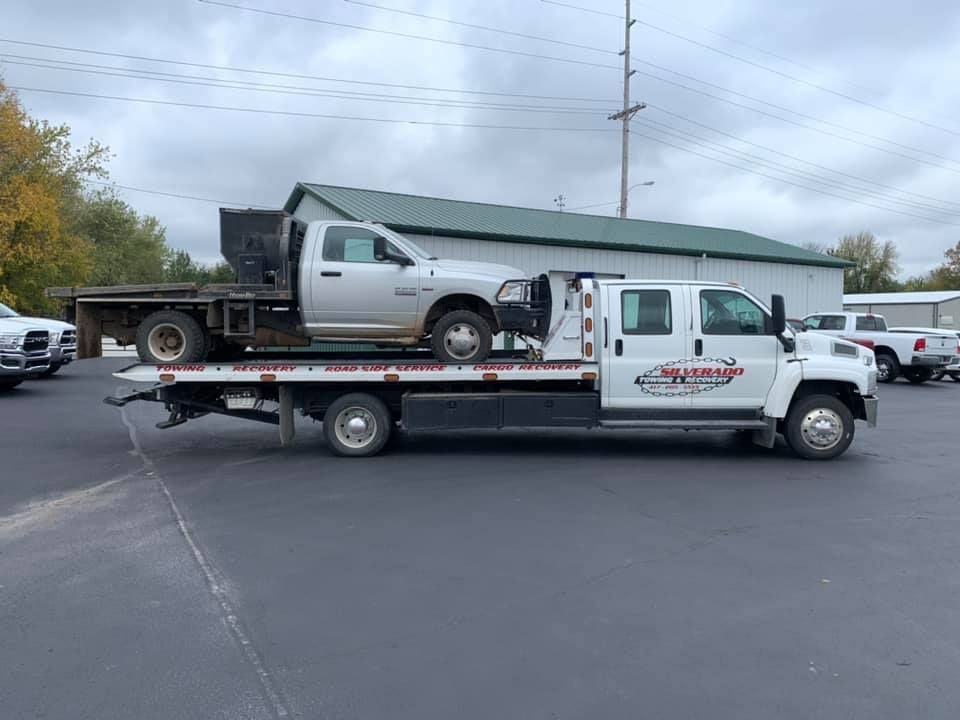 A tow truck is carrying a truck on the back of it.