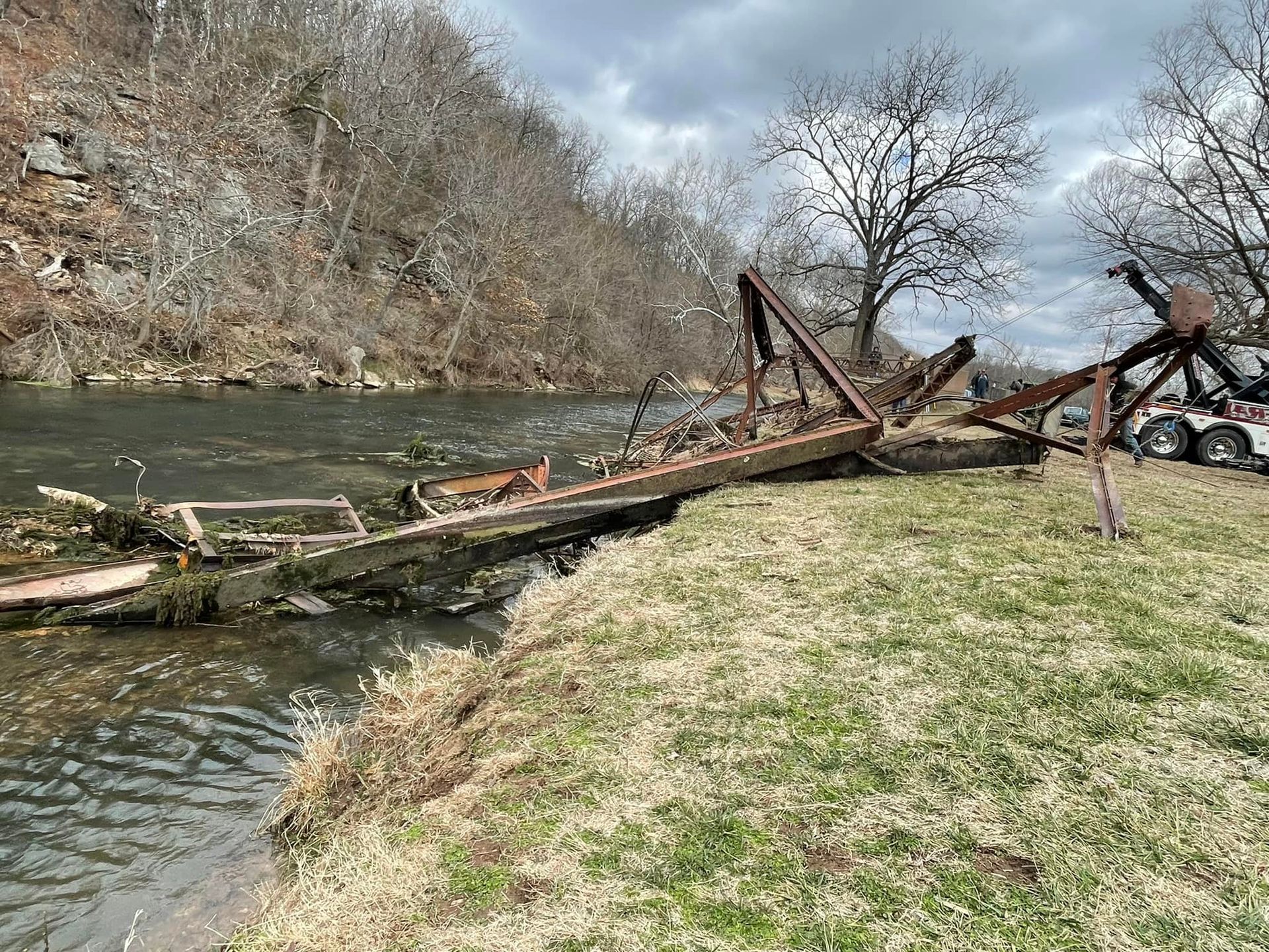A broken bridge is sitting on the shore of a river.