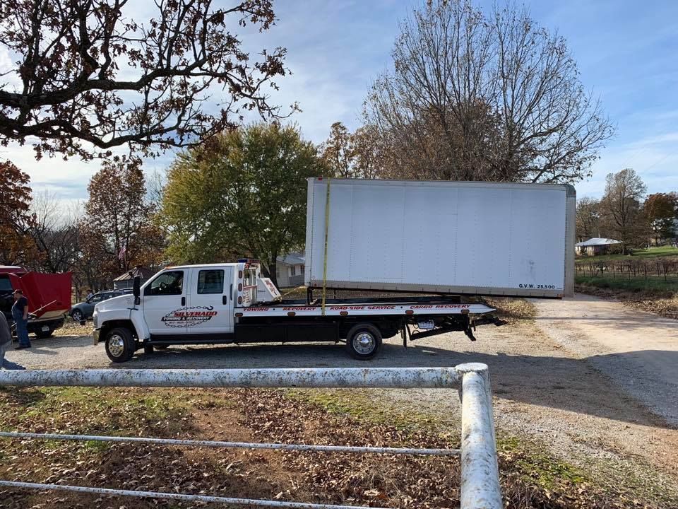A tow truck is carrying a large white box on the back of it.