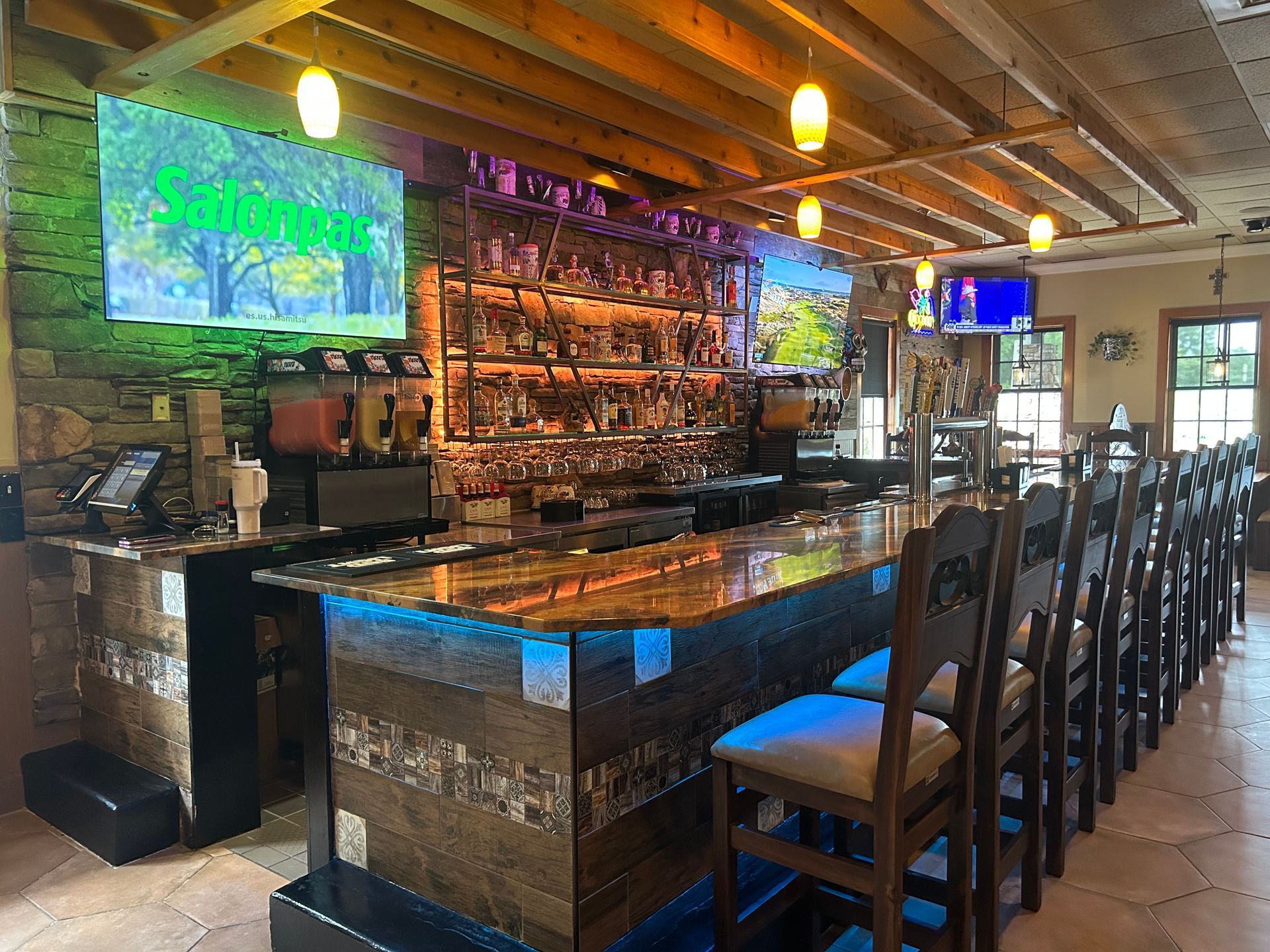 Bar interior with bar stools, liquor bottles, and televisions.