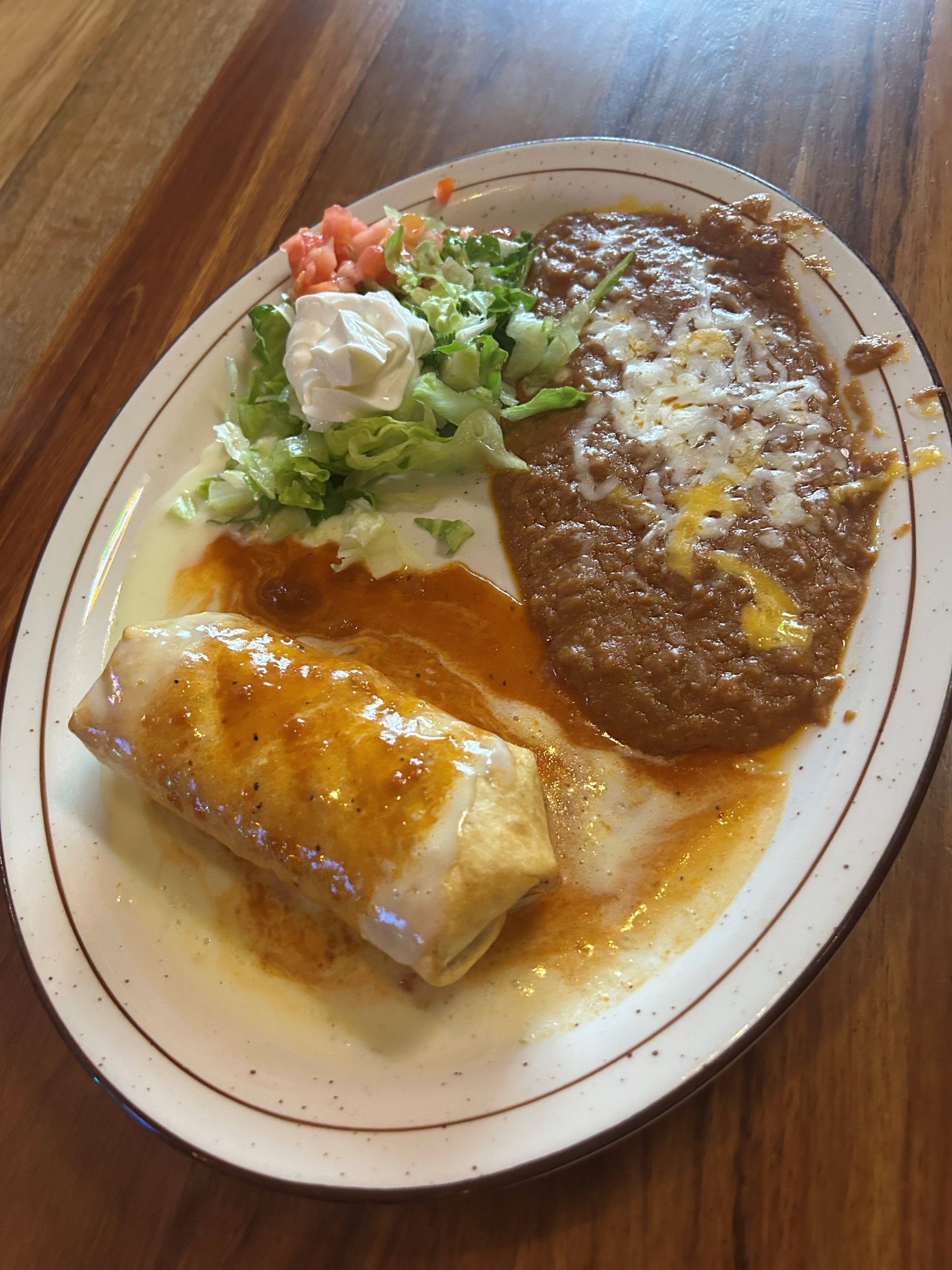 Burrito smothered in sauce with refried beans, lettuce, tomato, and sour cream on a plate.