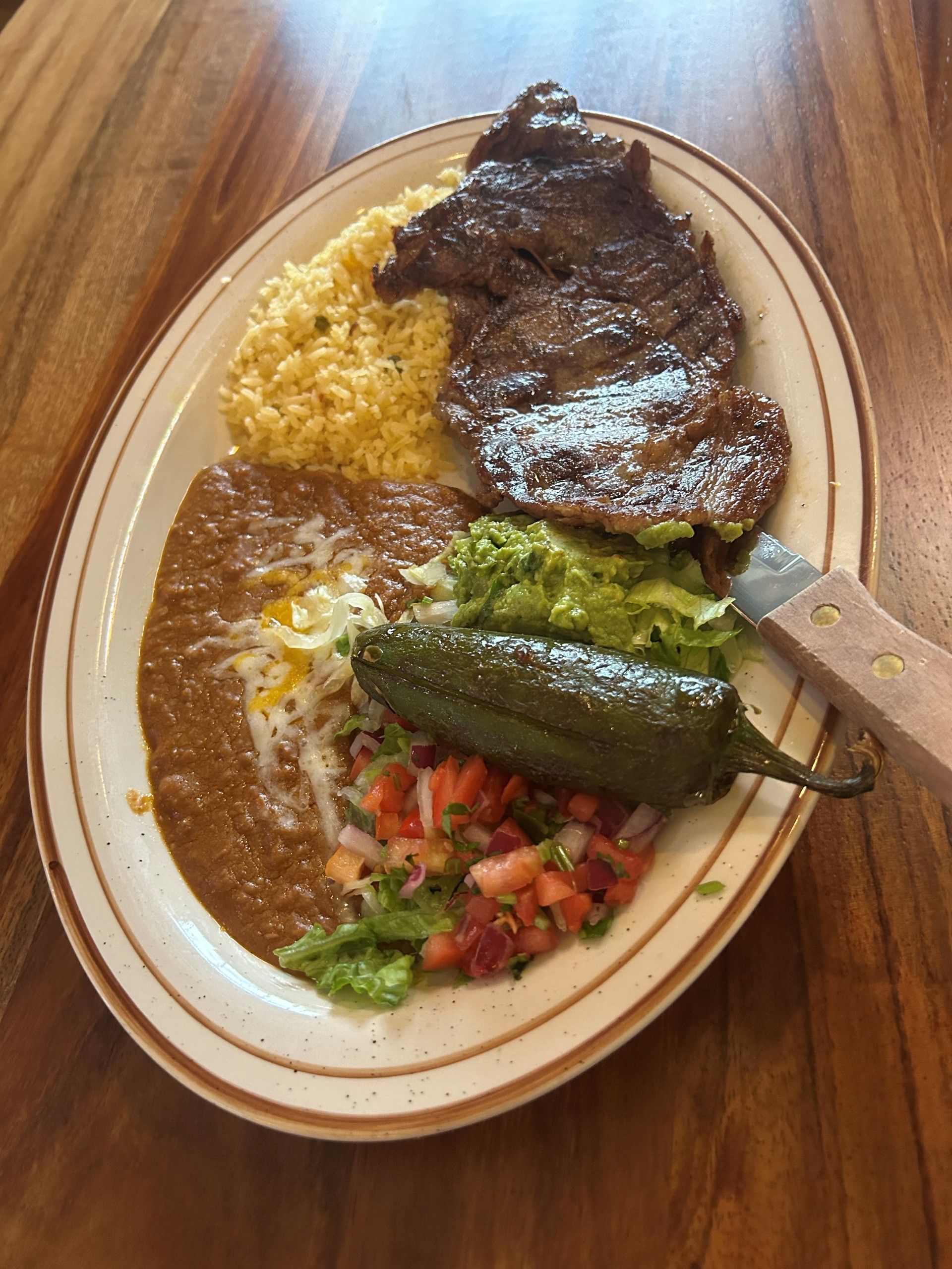 Plate of Mexican food: steak, rice, beans, guacamole, salsa, and a jalapeño.