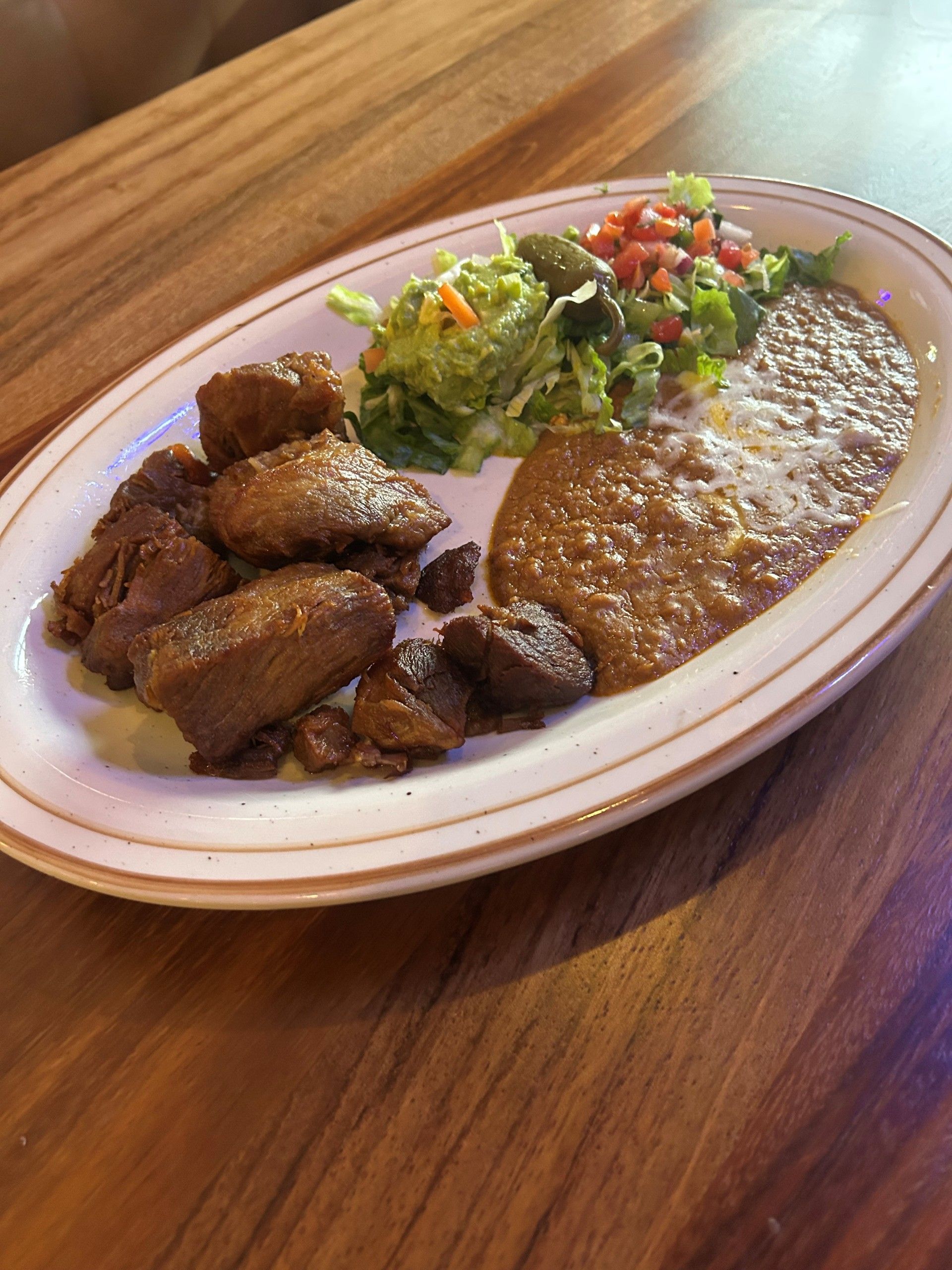 Plate with fried meat, refried beans, salad, and pico de gallo on a wooden table.