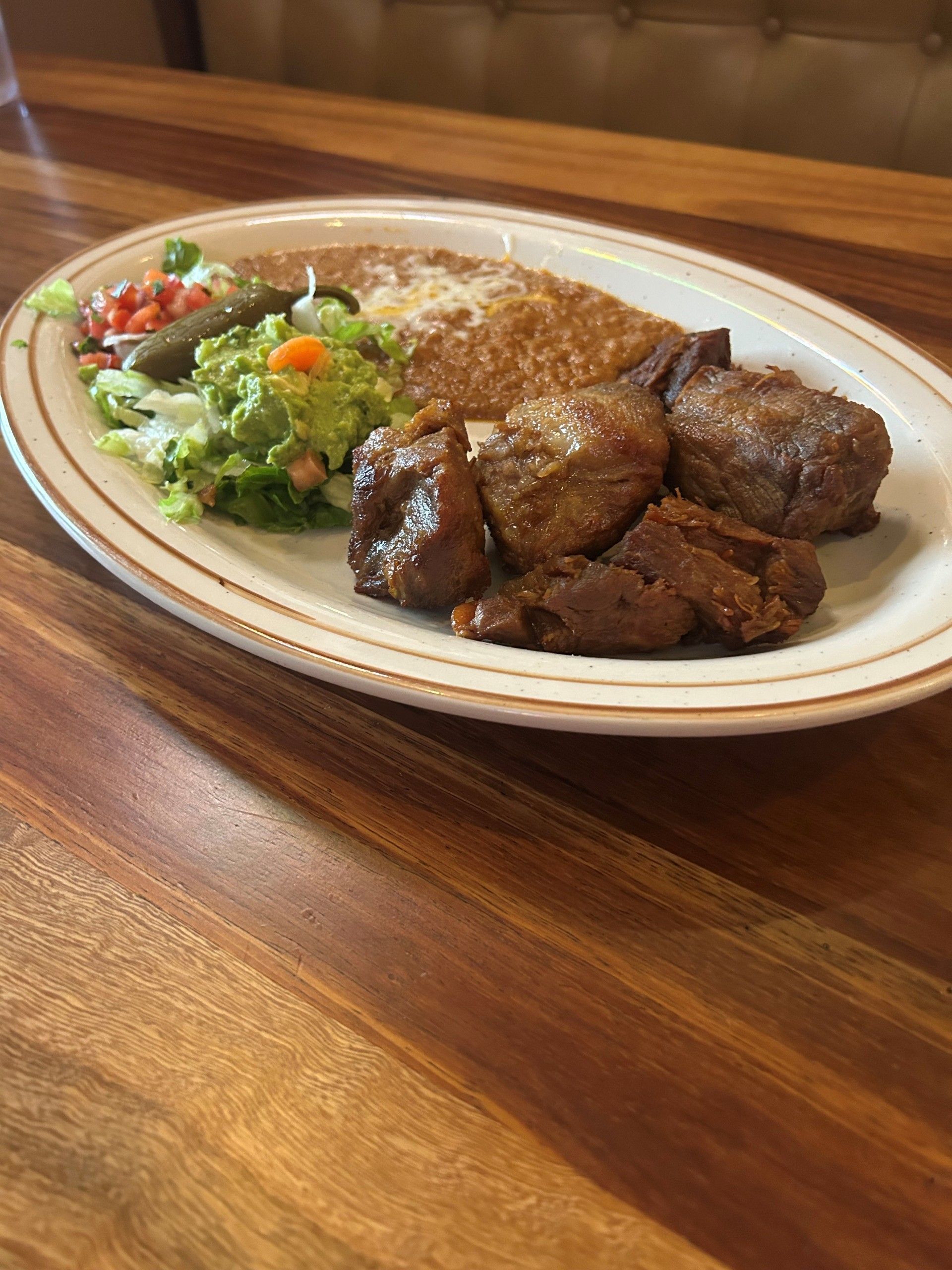 Plate of Mexican food on wooden table: enchiladas, guacamole, salsa, and meat.
