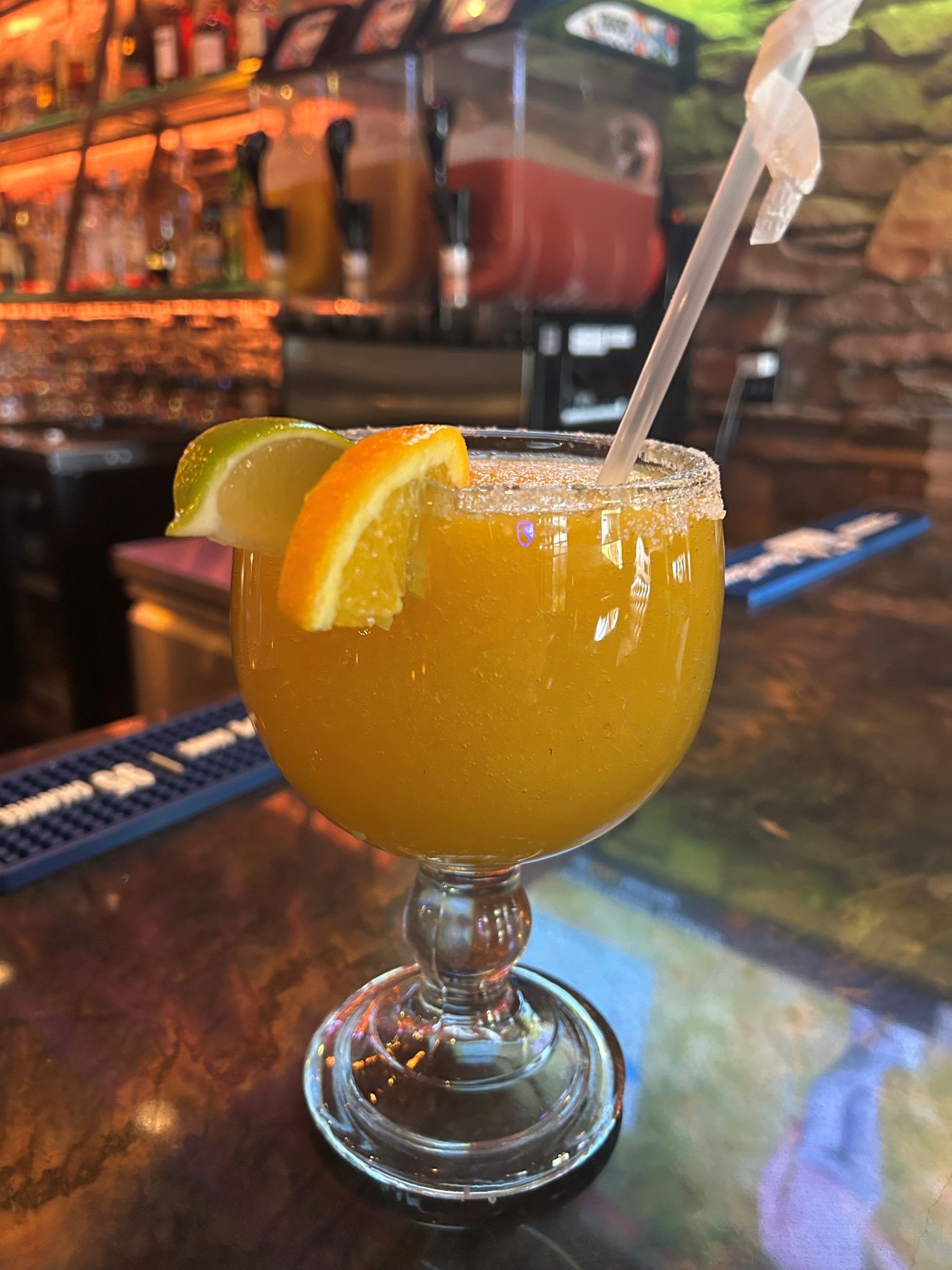 Mango margarita in a stemmed glass with lime and orange garnish, on a bar.