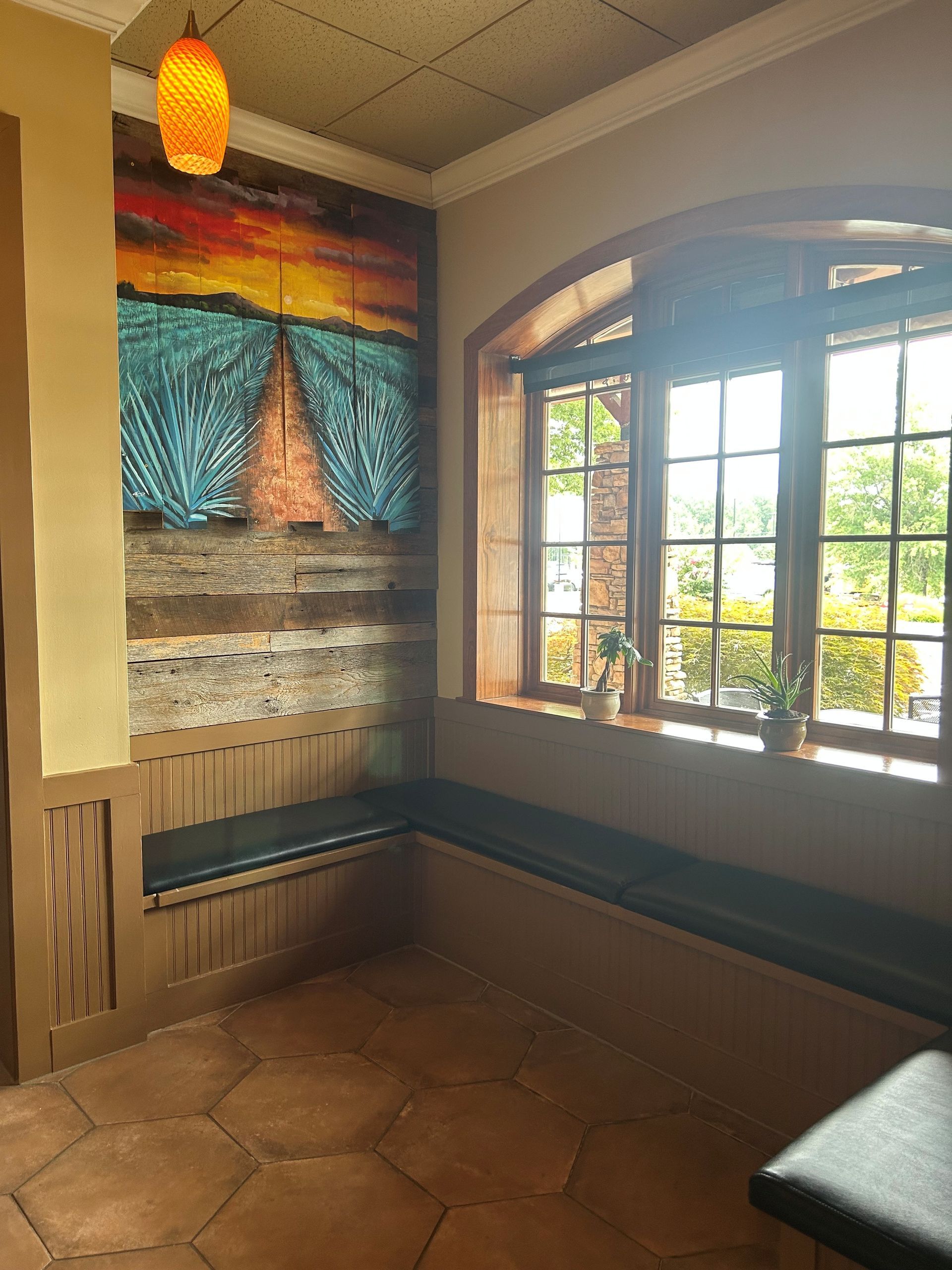 Cozy restaurant corner with built-in seating, artwork, and a window looking out onto greenery.
