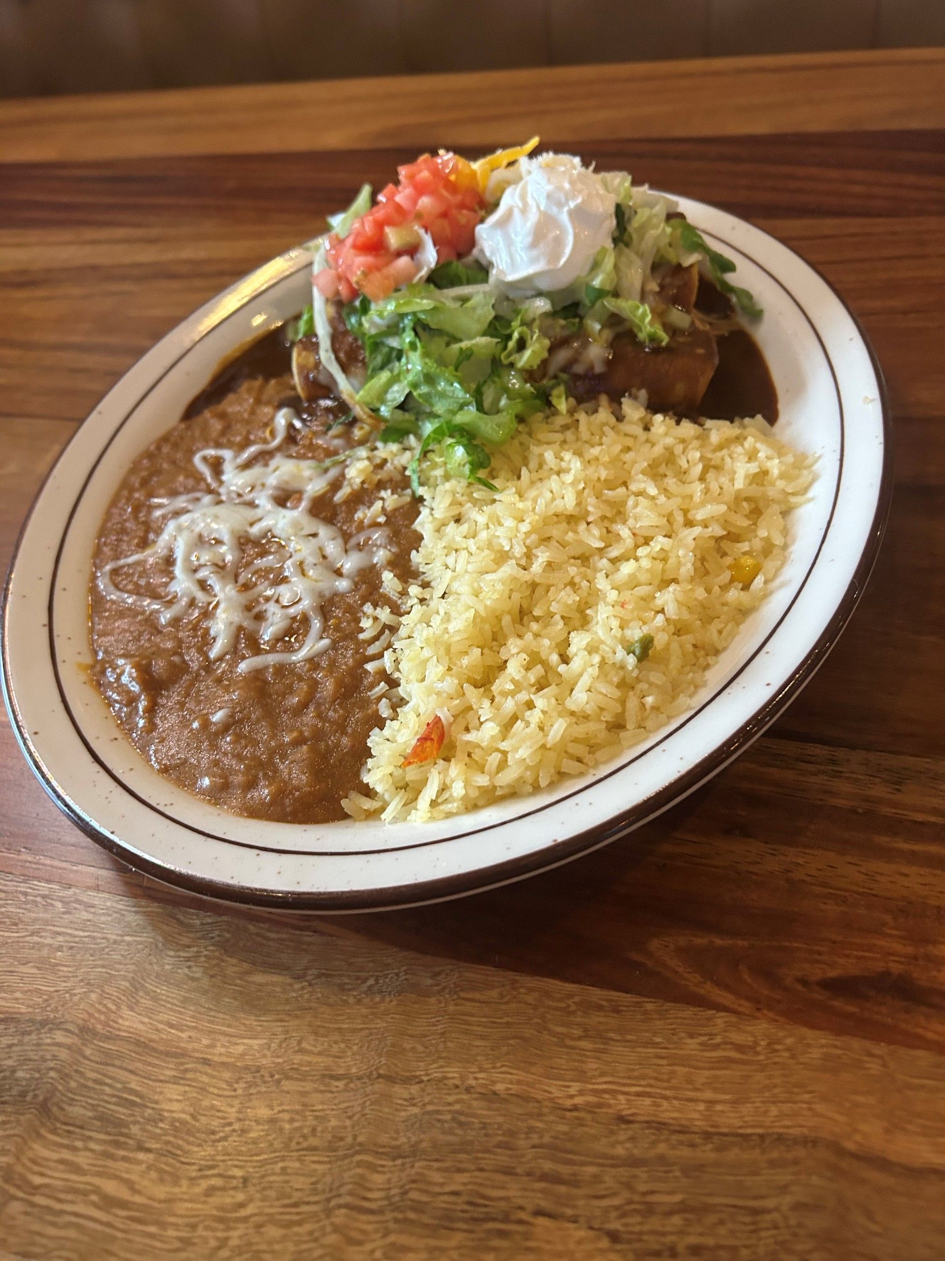 Plate of Mexican food: Enchilada, rice, beans, topped with lettuce, tomatoes, and sour cream.