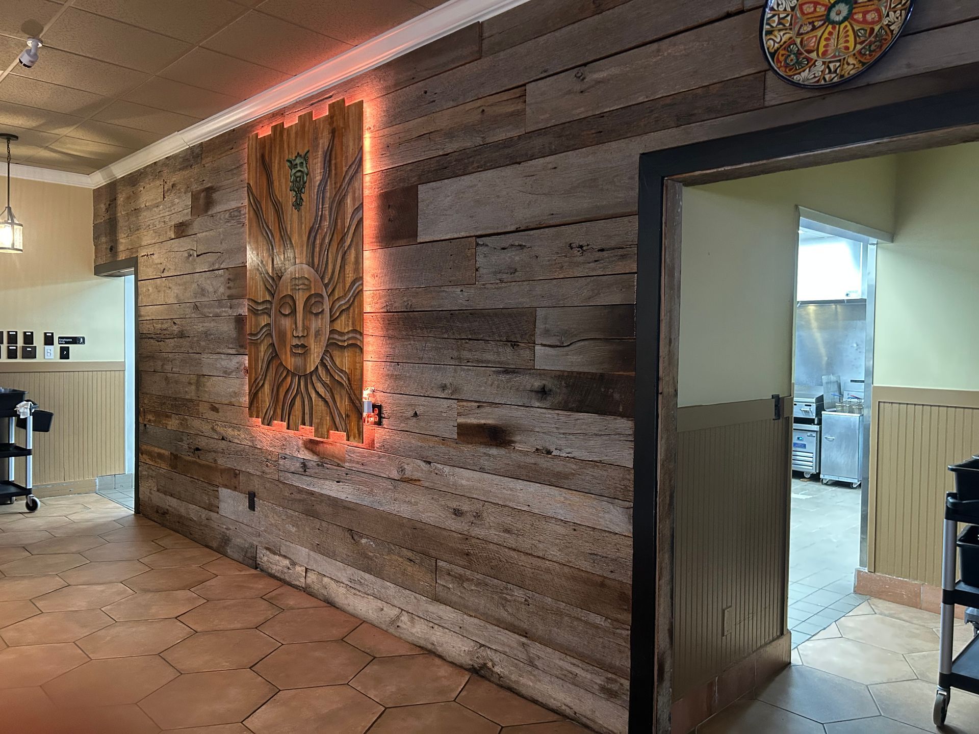 Wood-paneled wall with artwork and red backlighting. Doorway to kitchen with tile flooring.