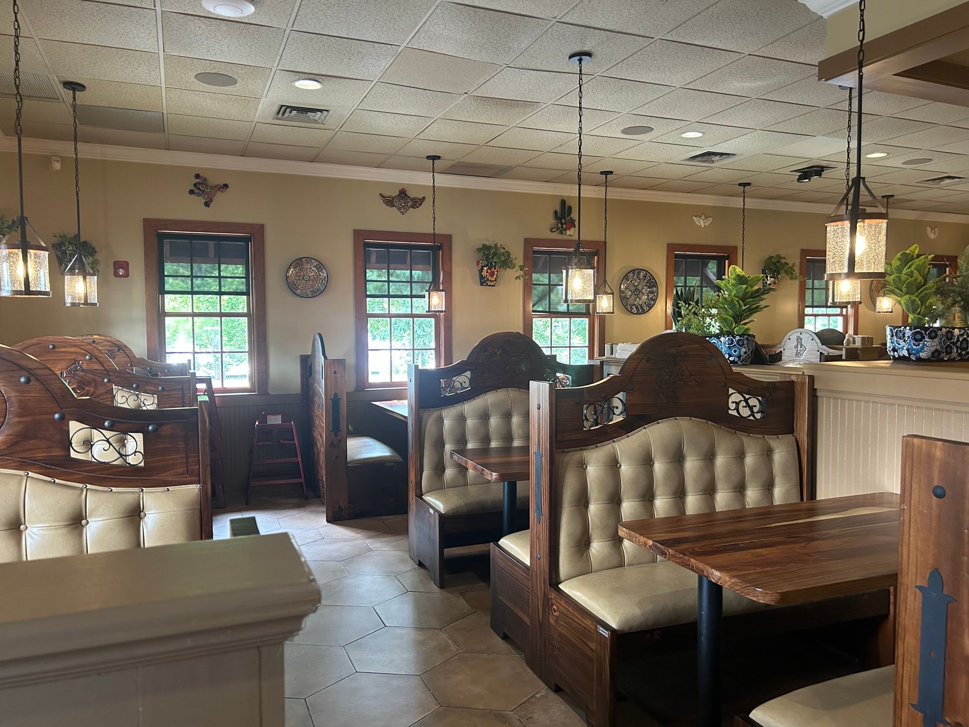 Interior of a restaurant with booths, wooden tables, pendant lights, and windows.