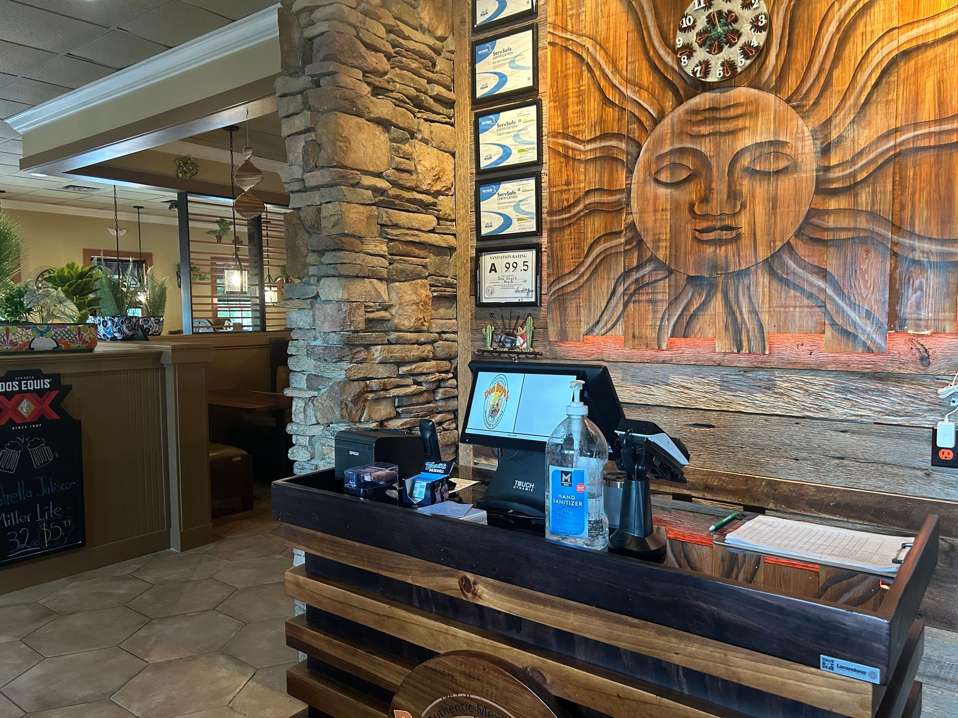 Restaurant interior with stone pillar, wooden sun carving, and a register counter.