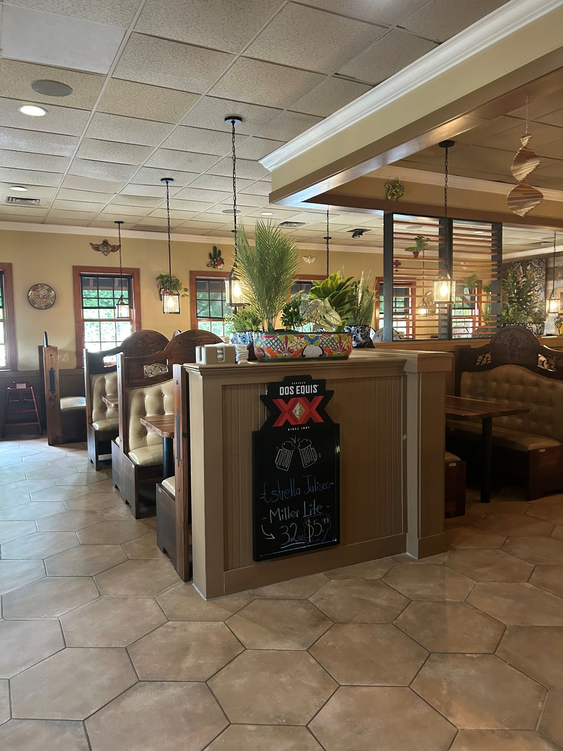 Interior of a Mexican restaurant with booths, hexagonal tiled floor, and a central counter with plants.