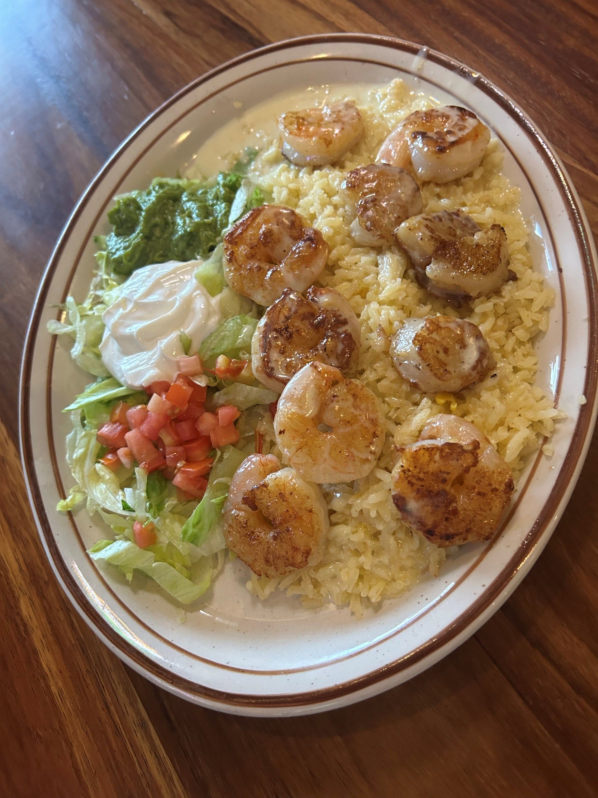 Seared shrimp over rice, with guacamole, sour cream, and diced tomatoes.