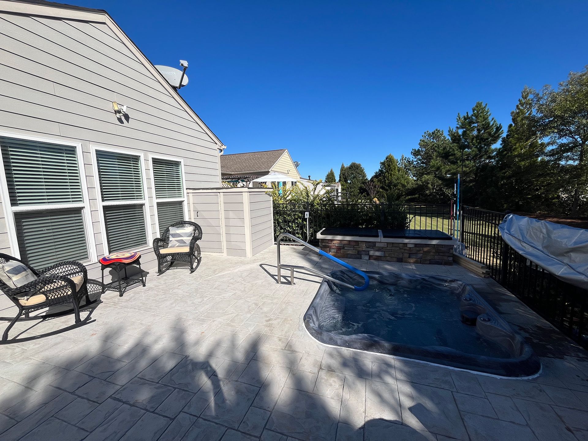 A patio with a hot tub and chairs in front of a house.