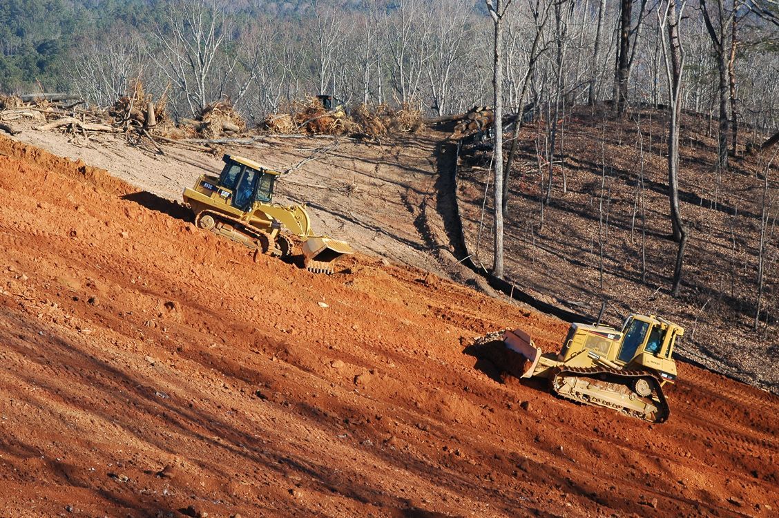 Two bulldozers are working on a dirt road in the woods.