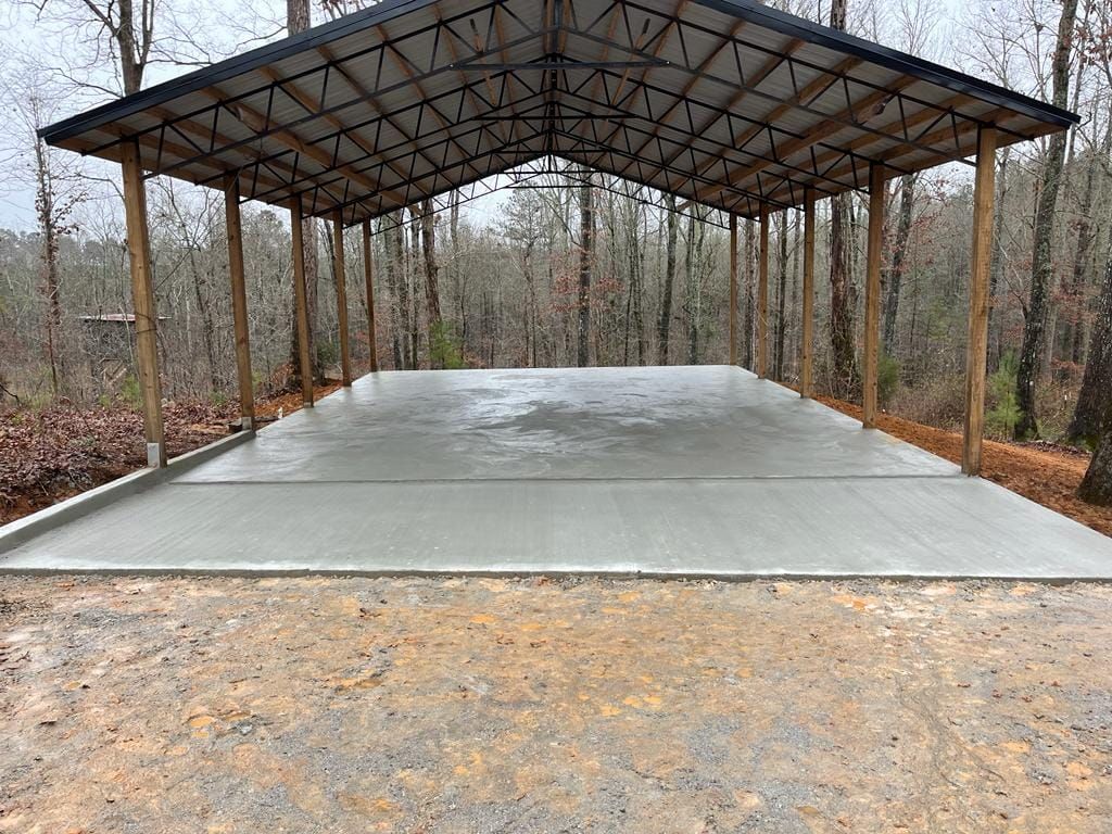 A large concrete garage with a metal roof in the middle of a forest.