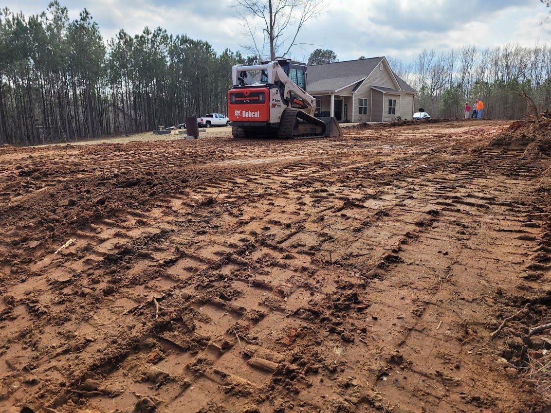 A bulldozer is working on a dirt road in front of a house.