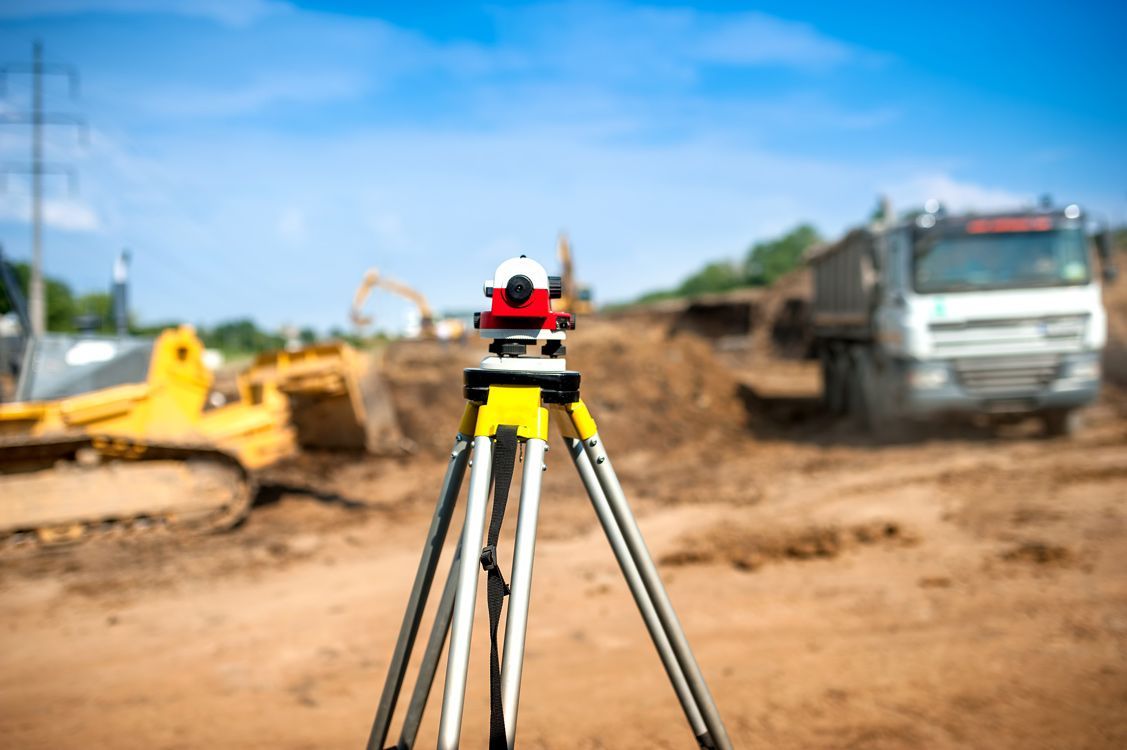 A surveyor's level is sitting on a tripod at a construction site.