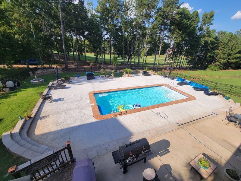 An aerial view of a large swimming pool in a backyard surrounded by trees.