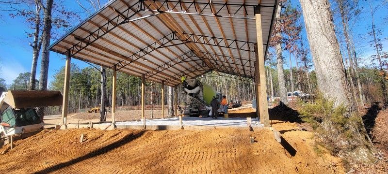 A concrete mixer is pouring concrete under a canopy in the woods.