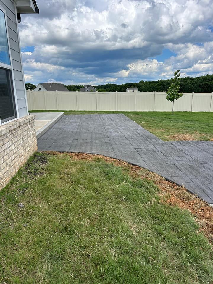 A concrete driveway leads to a house with a fence in the background.