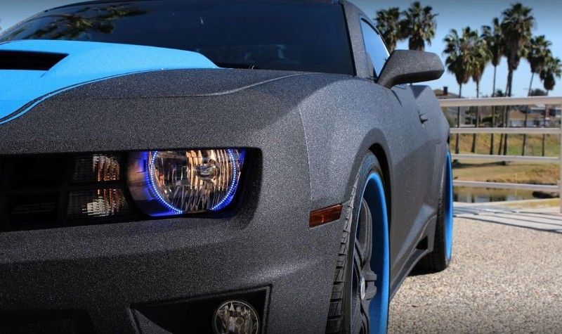 A black car with blue wheels is parked on the side of the road