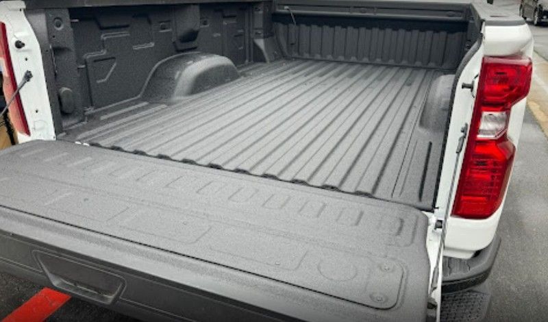 A white truck with a black bed is parked in a parking lot.