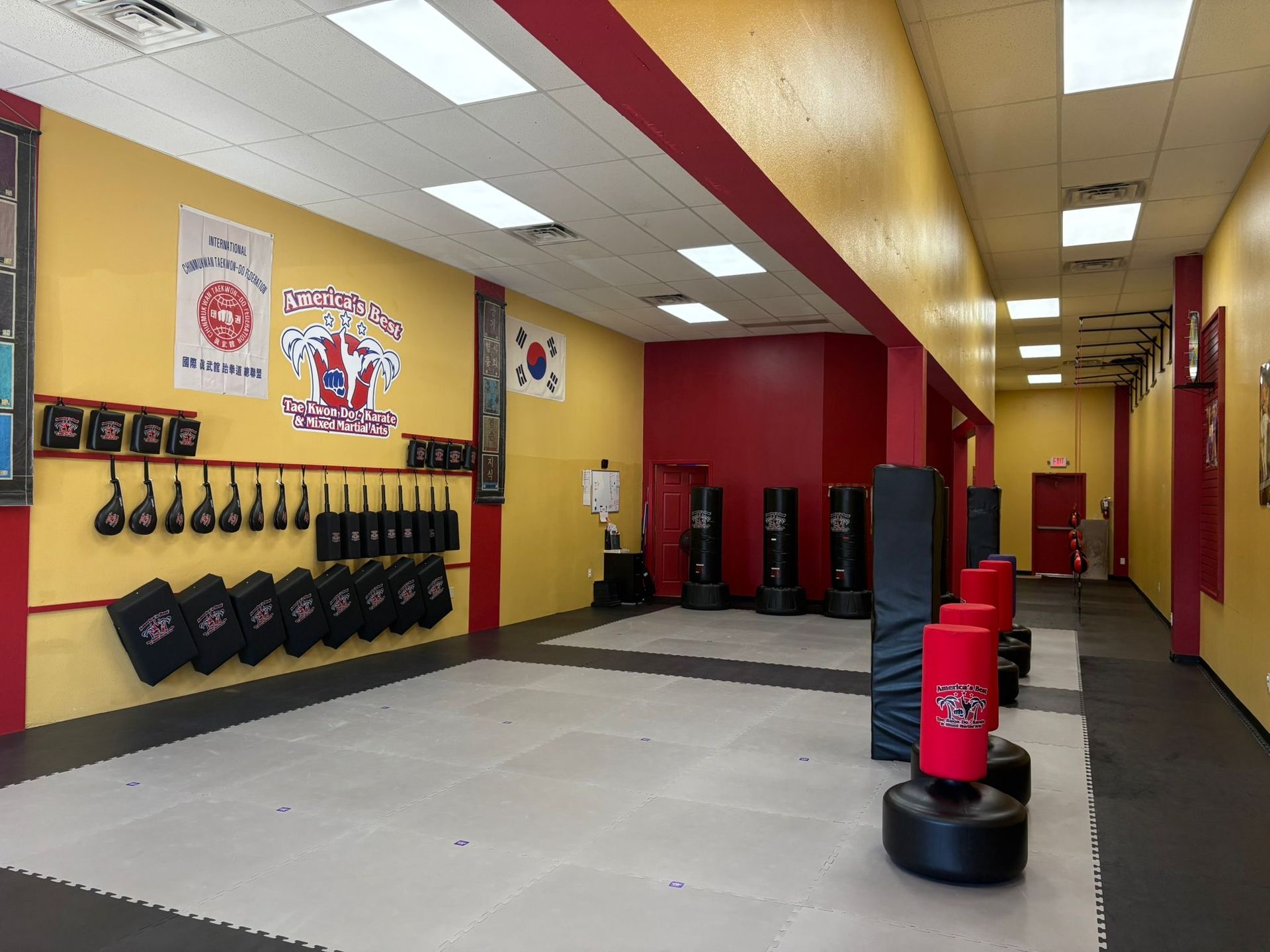 Martial arts studio interior with punching bags, yellow and red walls, and mats.