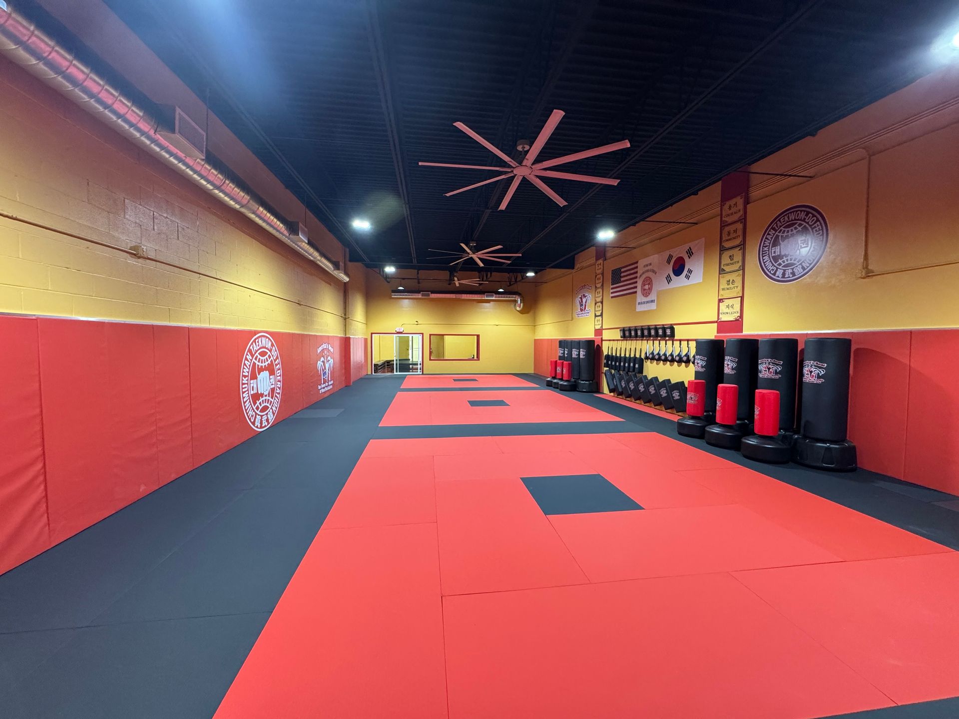Martial arts training room with red and black mats, heavy bags, and yellow walls.
