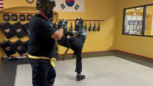 Two people practicing martial arts in a dojo. One person kicks while the other blocks.