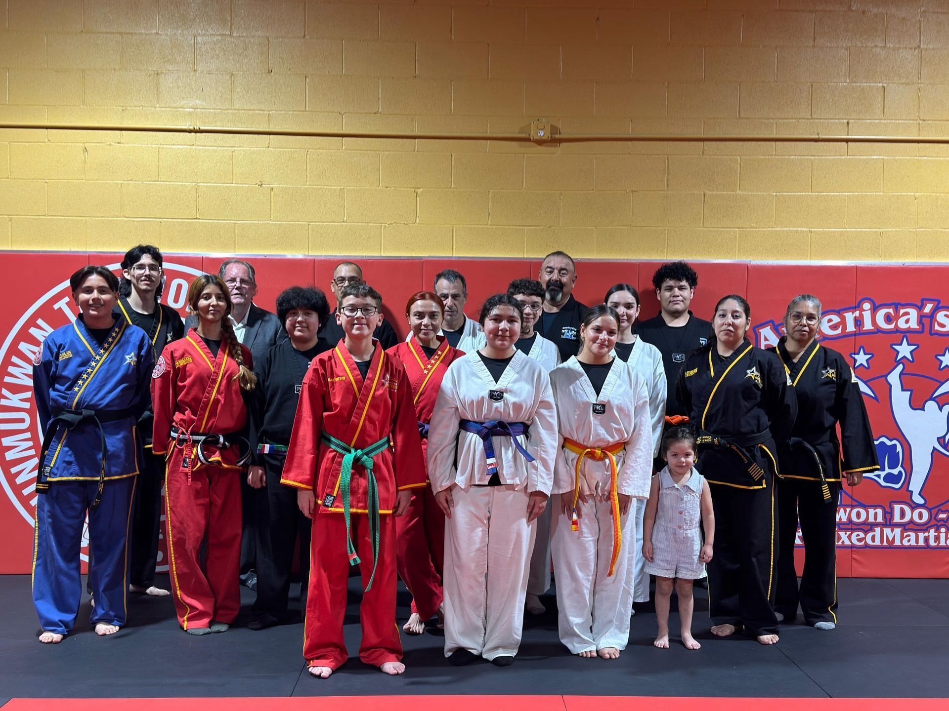 Children in black uniforms practice martial arts kicks in a gym.