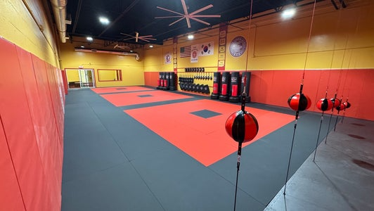 Three people in karate uniforms practicing a stance in a dojo.