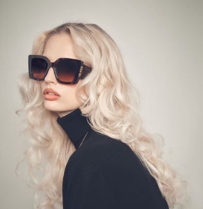 Blonde person in oversized black sunglasses and turtleneck against a light background