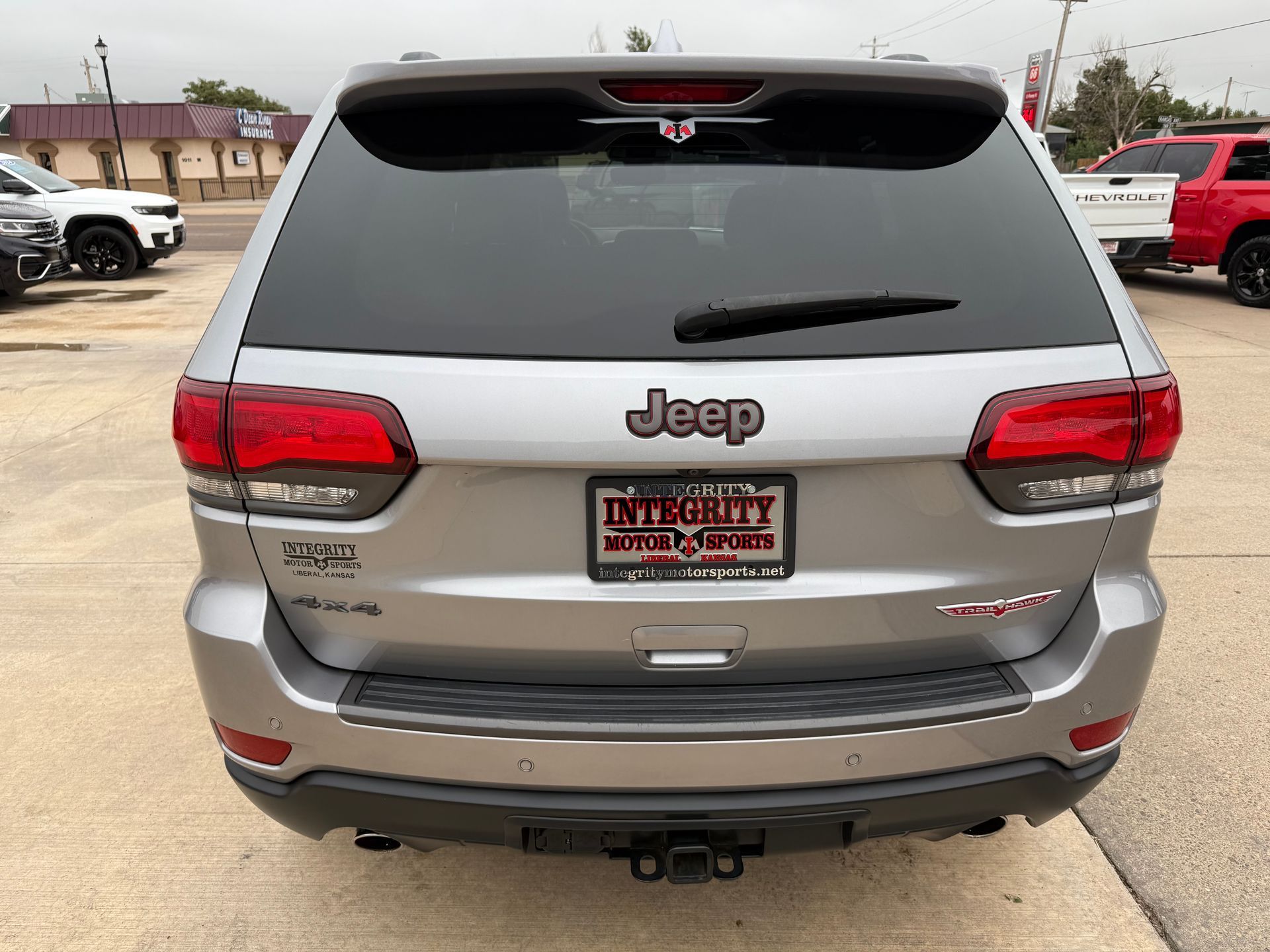 Rear view of a silver Jeep Grand Cherokee at a car dealership.