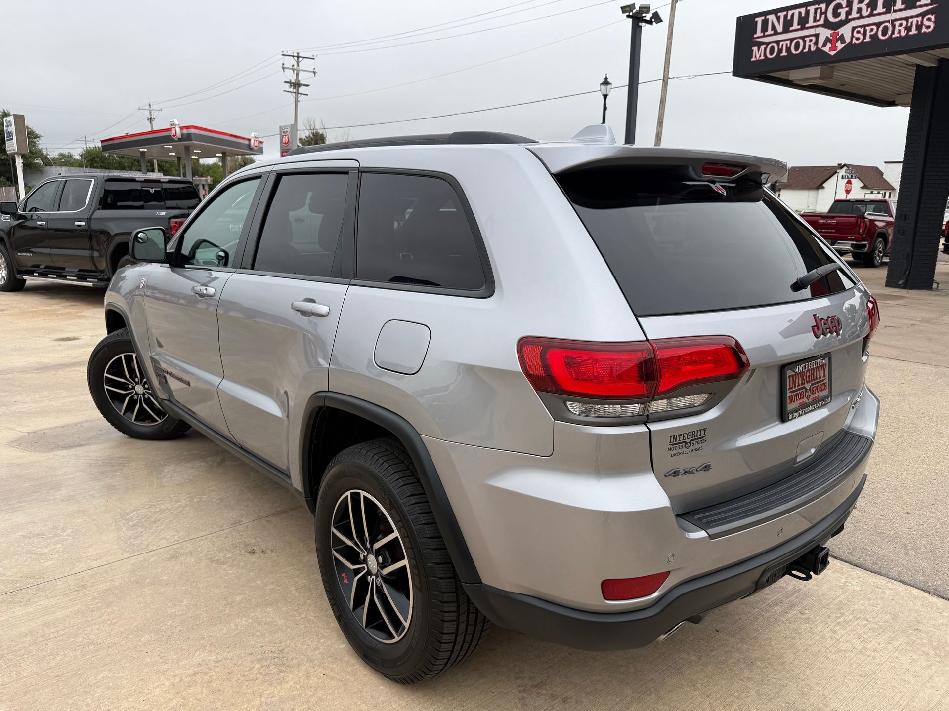 Silver Jeep Grand Cherokee parked outside a business. Black wheels, tinted windows.