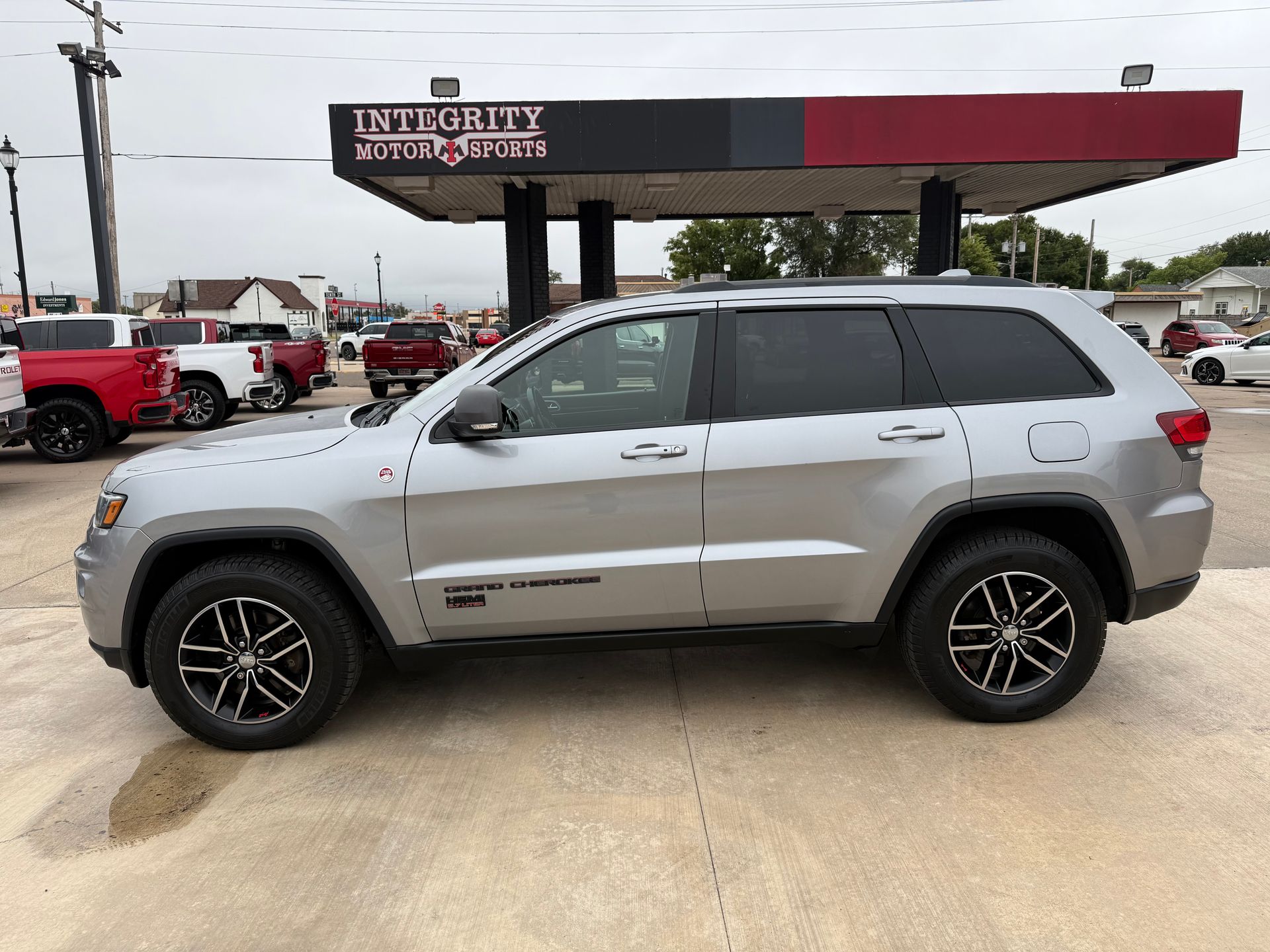 Silver Jeep SUV parked at a car dealership with black and red accents.
