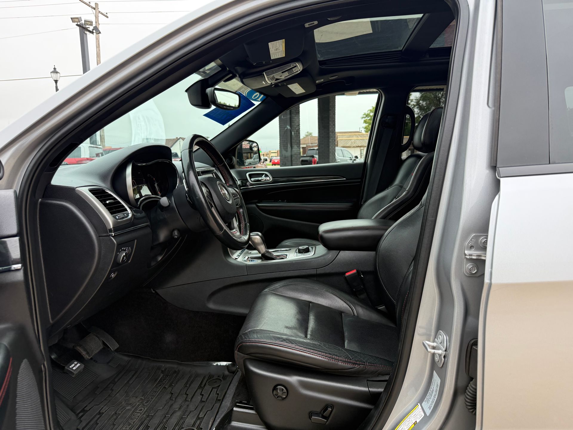 Interior of a gray Jeep with black leather seats, open door, sun roof, steering wheel visible.