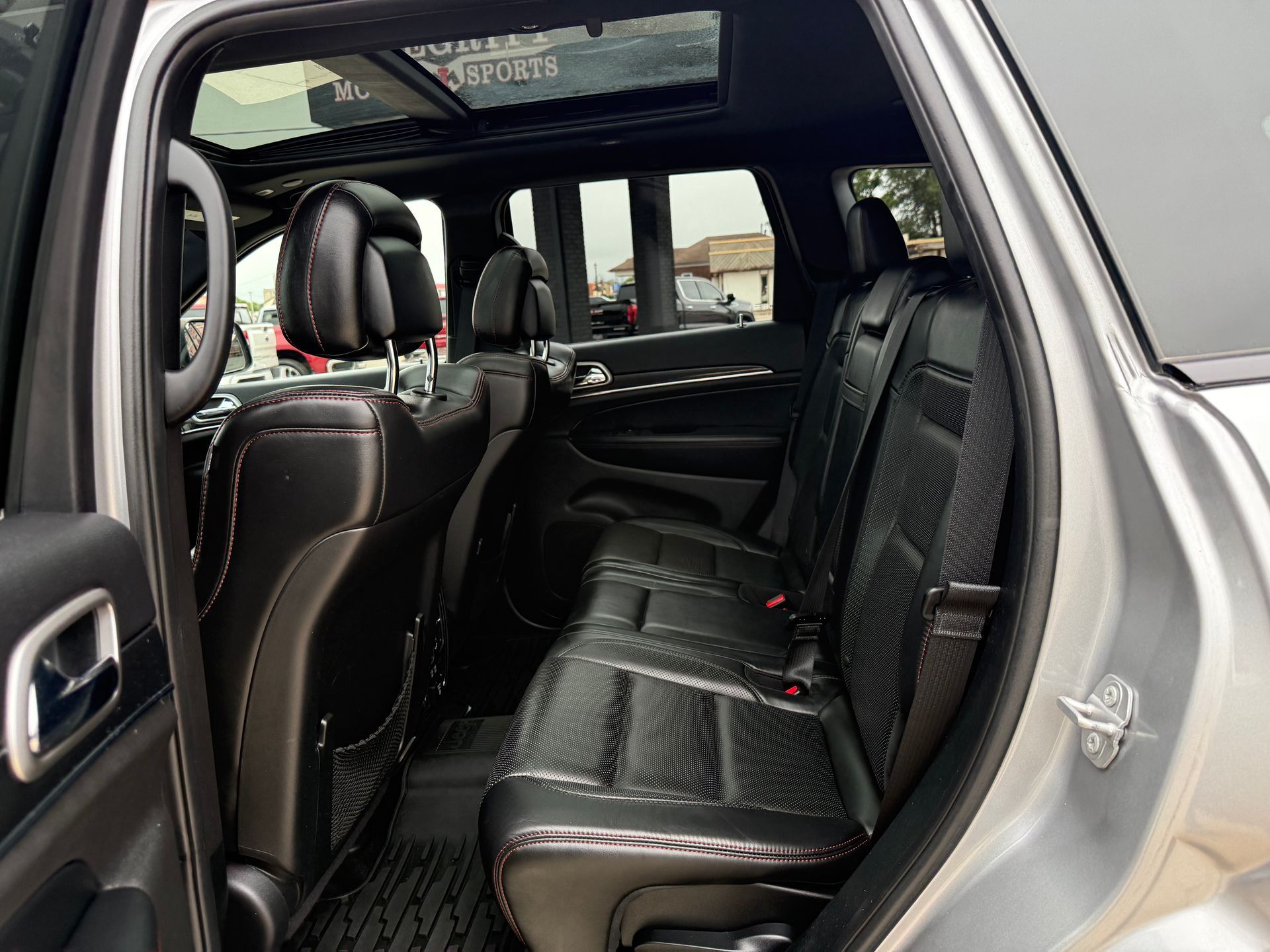 Interior view of a silver Jeep Grand Cherokee's back seats; black leather seats, tinted windows, and a sunroof.