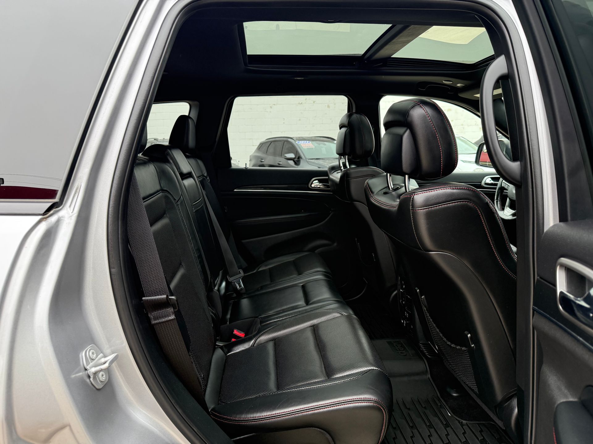 Back interior of a silver SUV, showcasing black leather seats, a sunroof, and a rear door open.