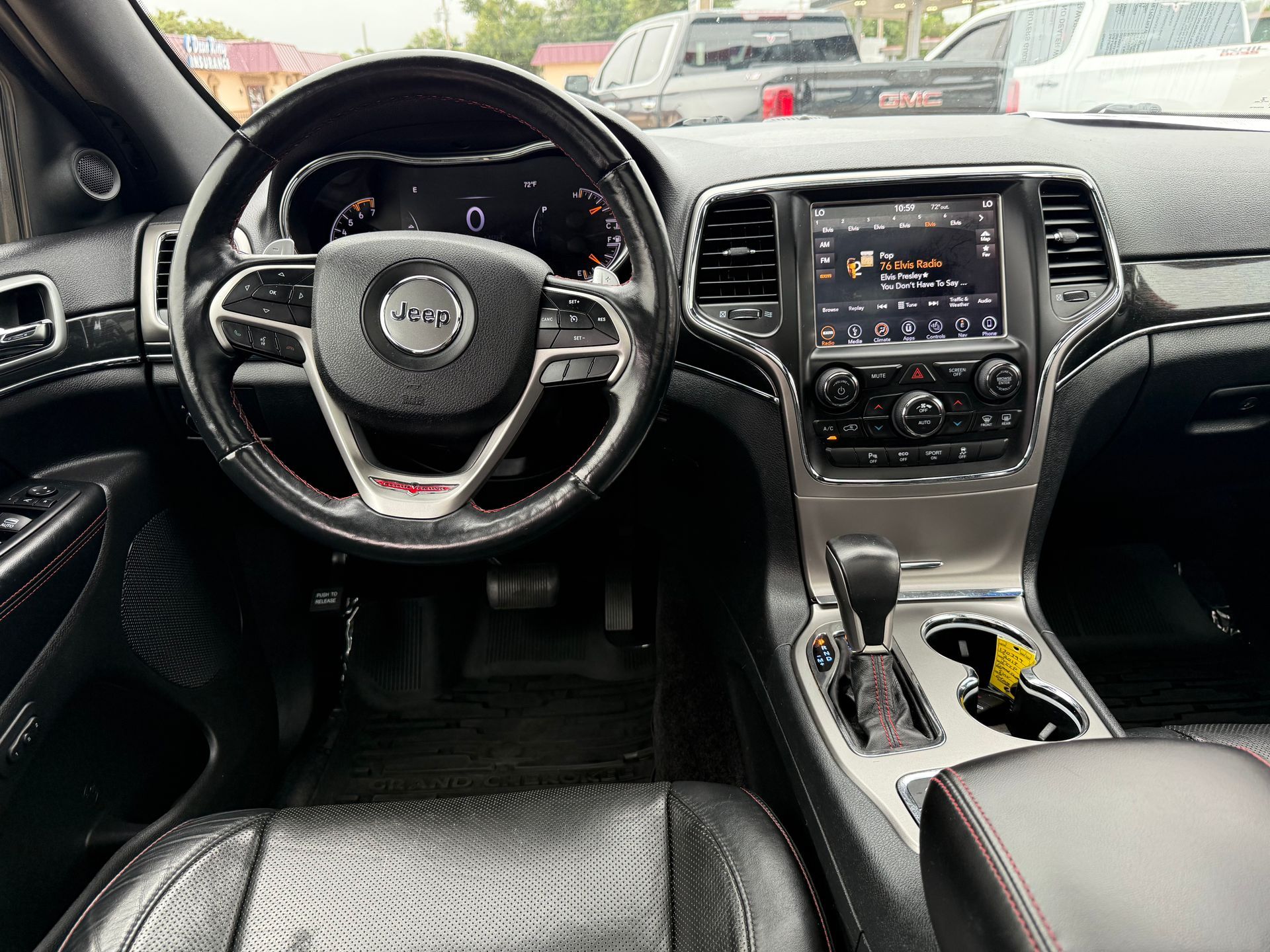 Interior view of a Jeep Grand Cherokee dashboard, black and silver with a touch screen and steering wheel with red accents.