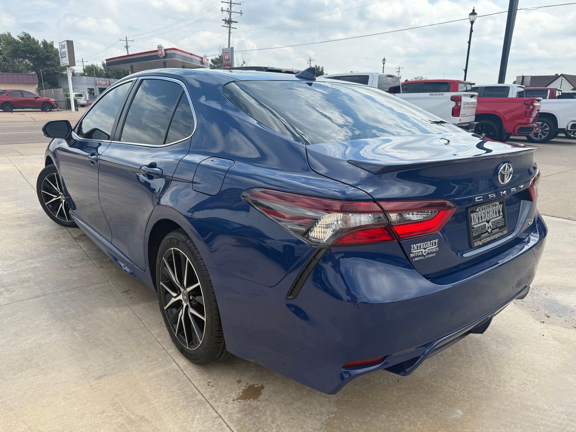 Blue Toyota Camry sedan, rear view, parked on concrete, sunny day.