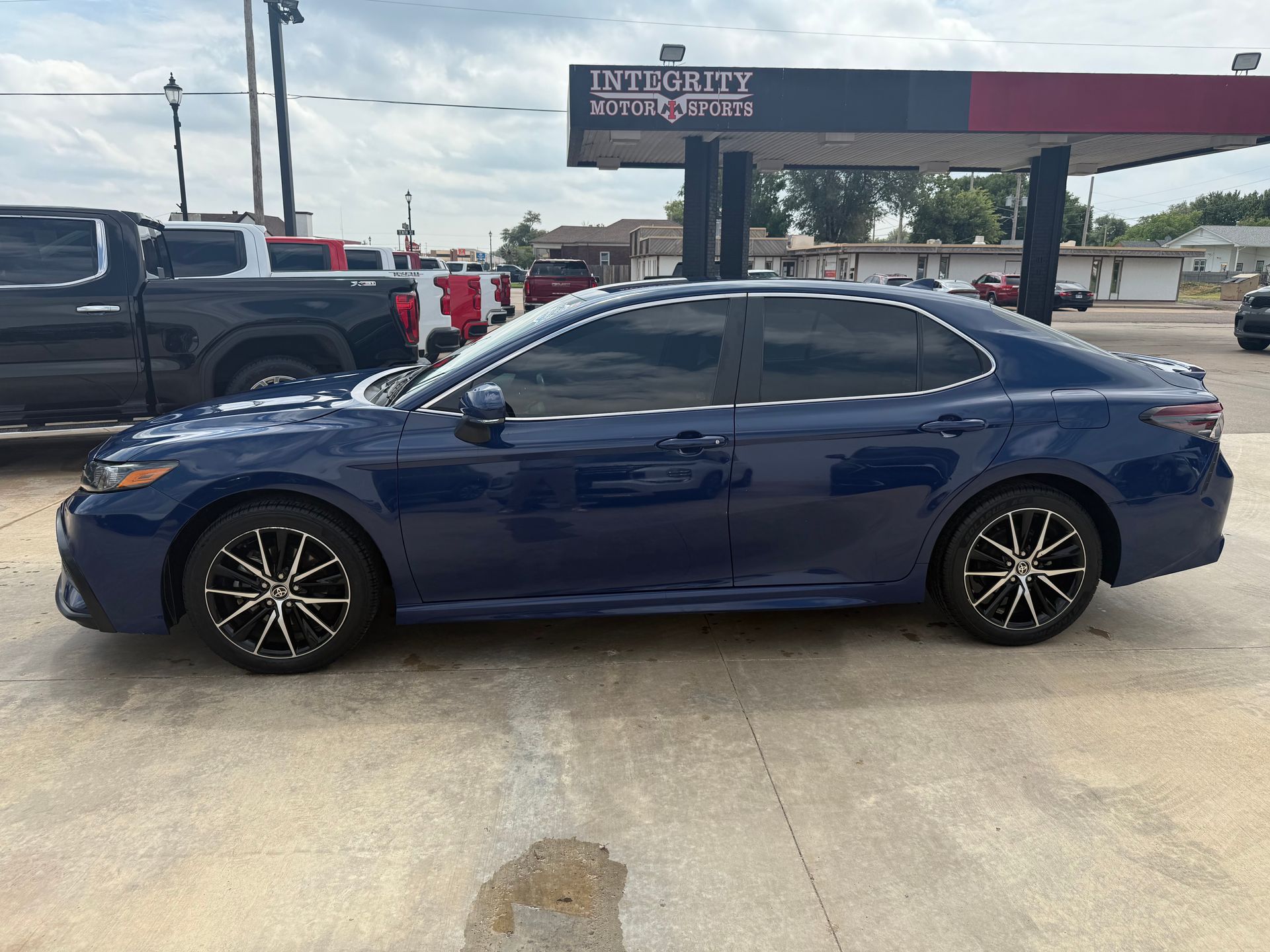 Blue sedan parked near a gas station. Black rims, tinted windows, overcast sky.