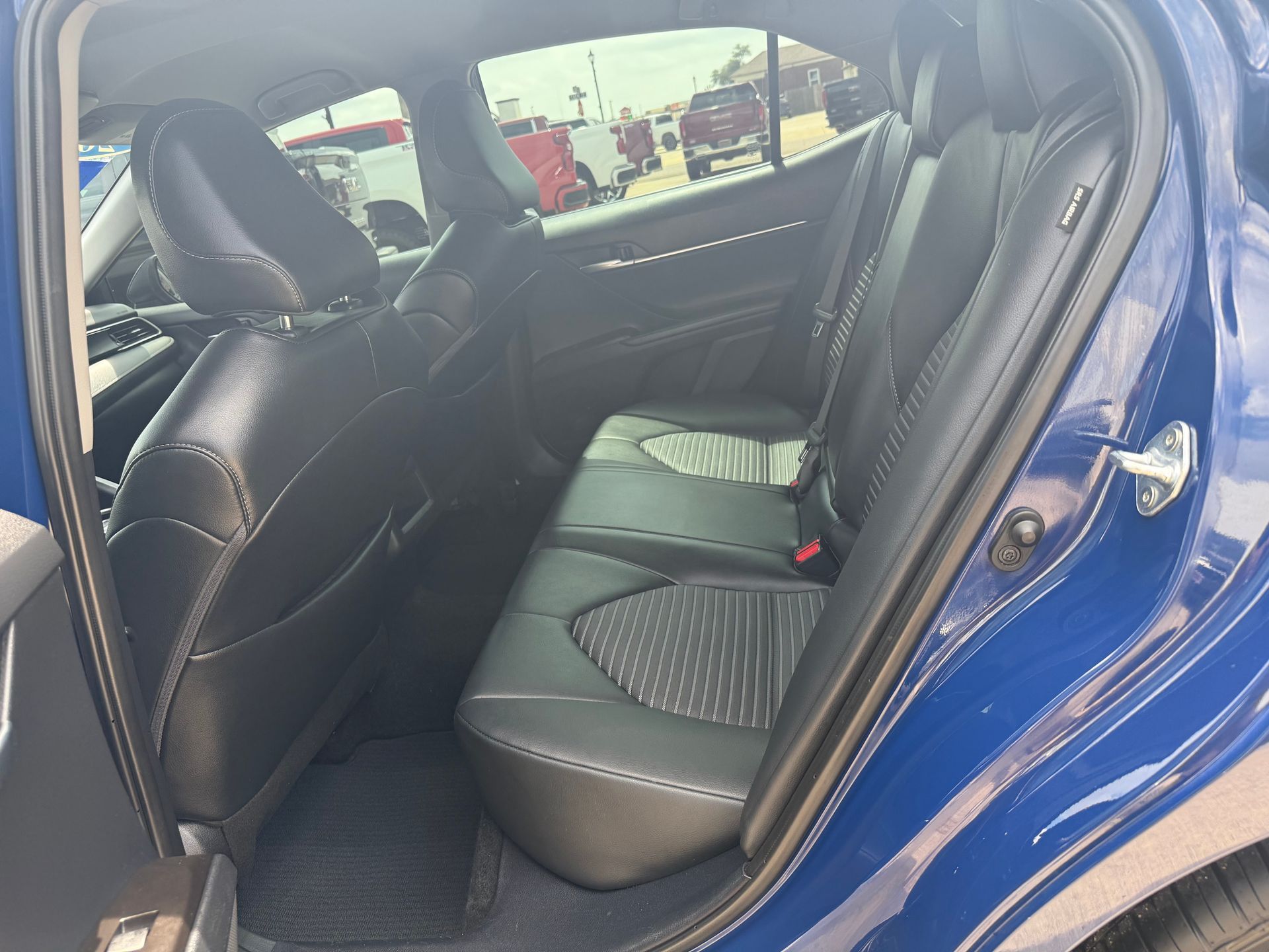 Blue car interior, rear seats: black leather, clean. Outdoors, sunlight.