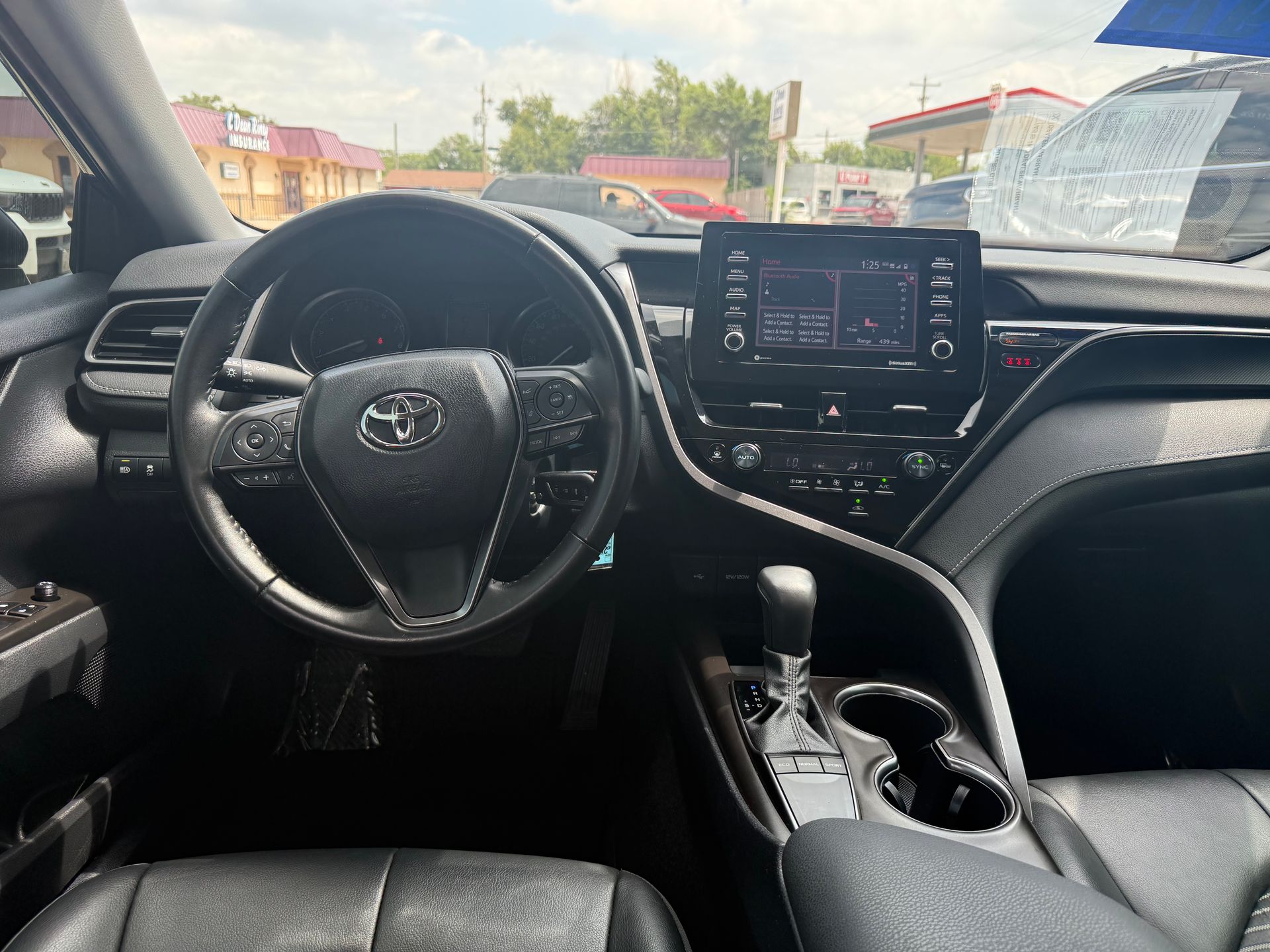 Black Toyota Camry interior: steering wheel, dashboard with infotainment screen, gear shift, and cup holders.