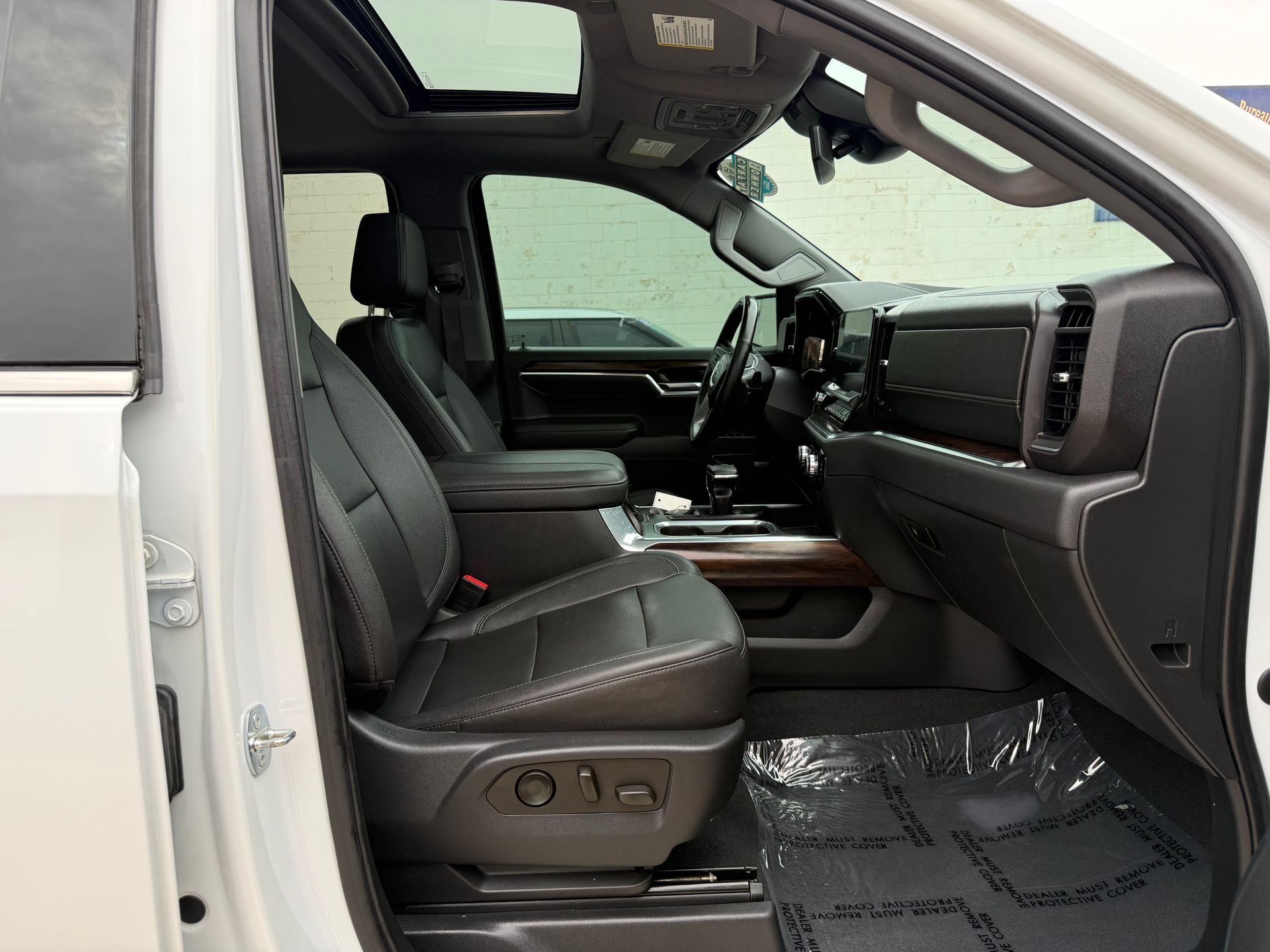 Interior view of a white truck with black leather seats, a sunroof, and clear floor mats.