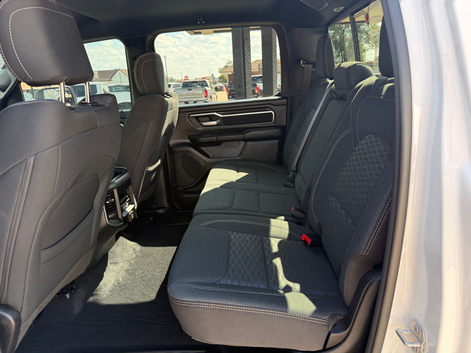 Interior of a silver truck's back seat, black cloth seats, sunlight through the window.