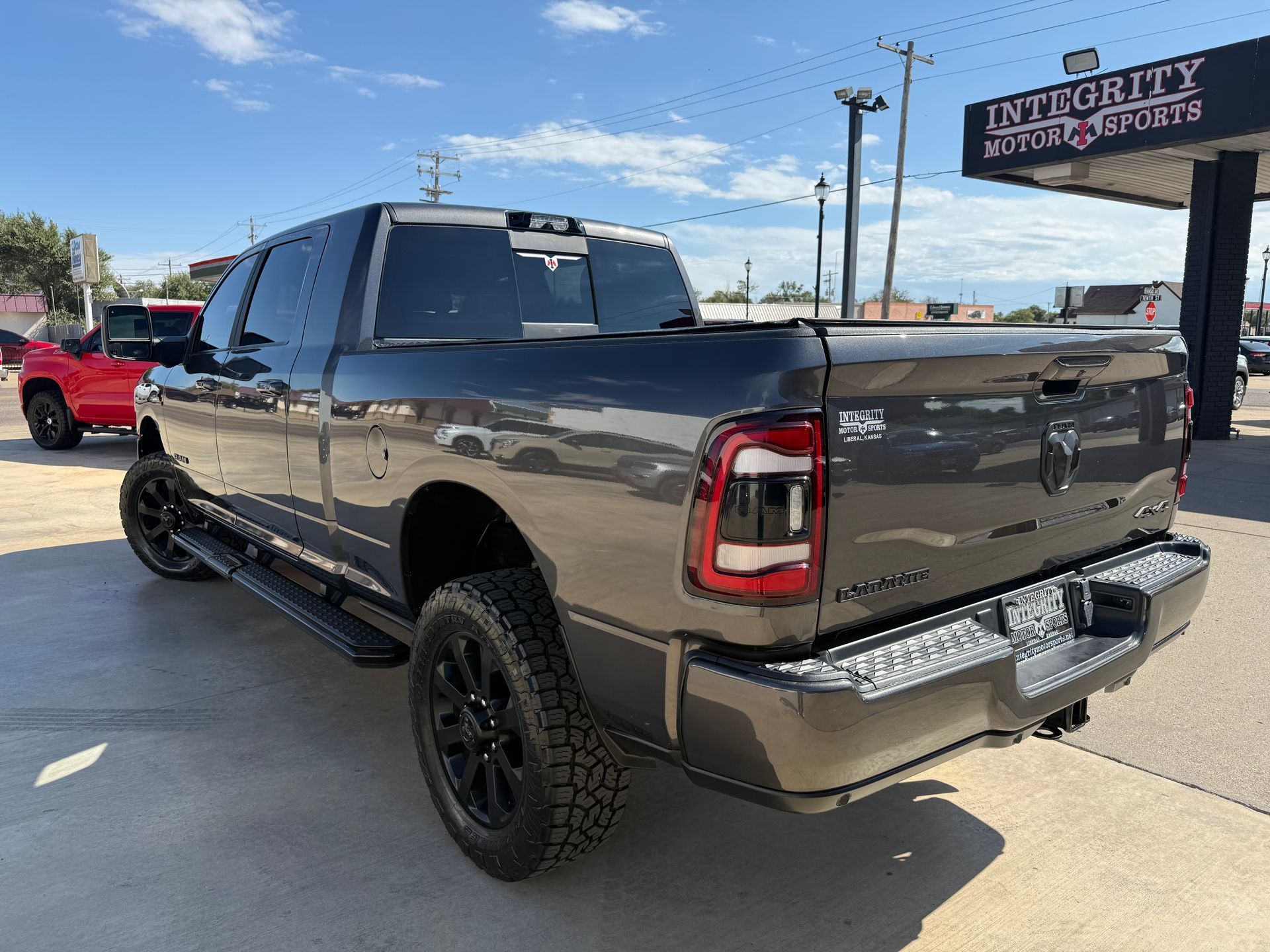 Dark gray Ram pickup truck parked outside a dealership, black wheels, sunny day.