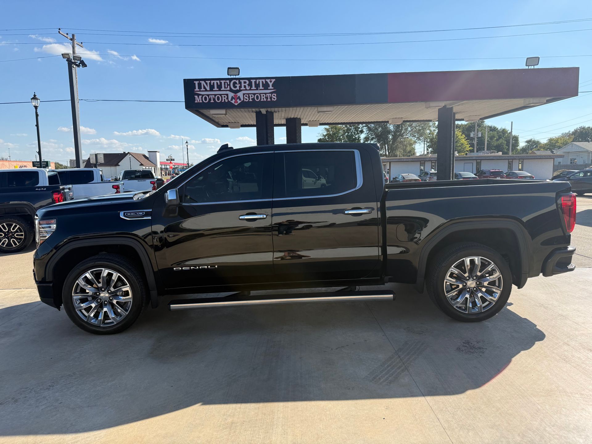 Black GMC pickup truck parked under a gas station canopy on a sunny day.