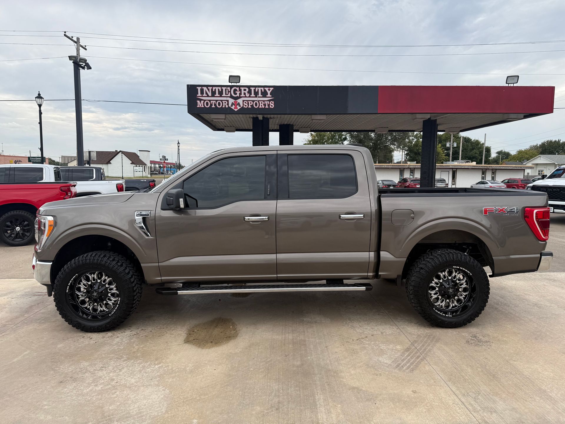 Brown Ford F-150 truck parked with black rims at a gas station under a cloudy sky.