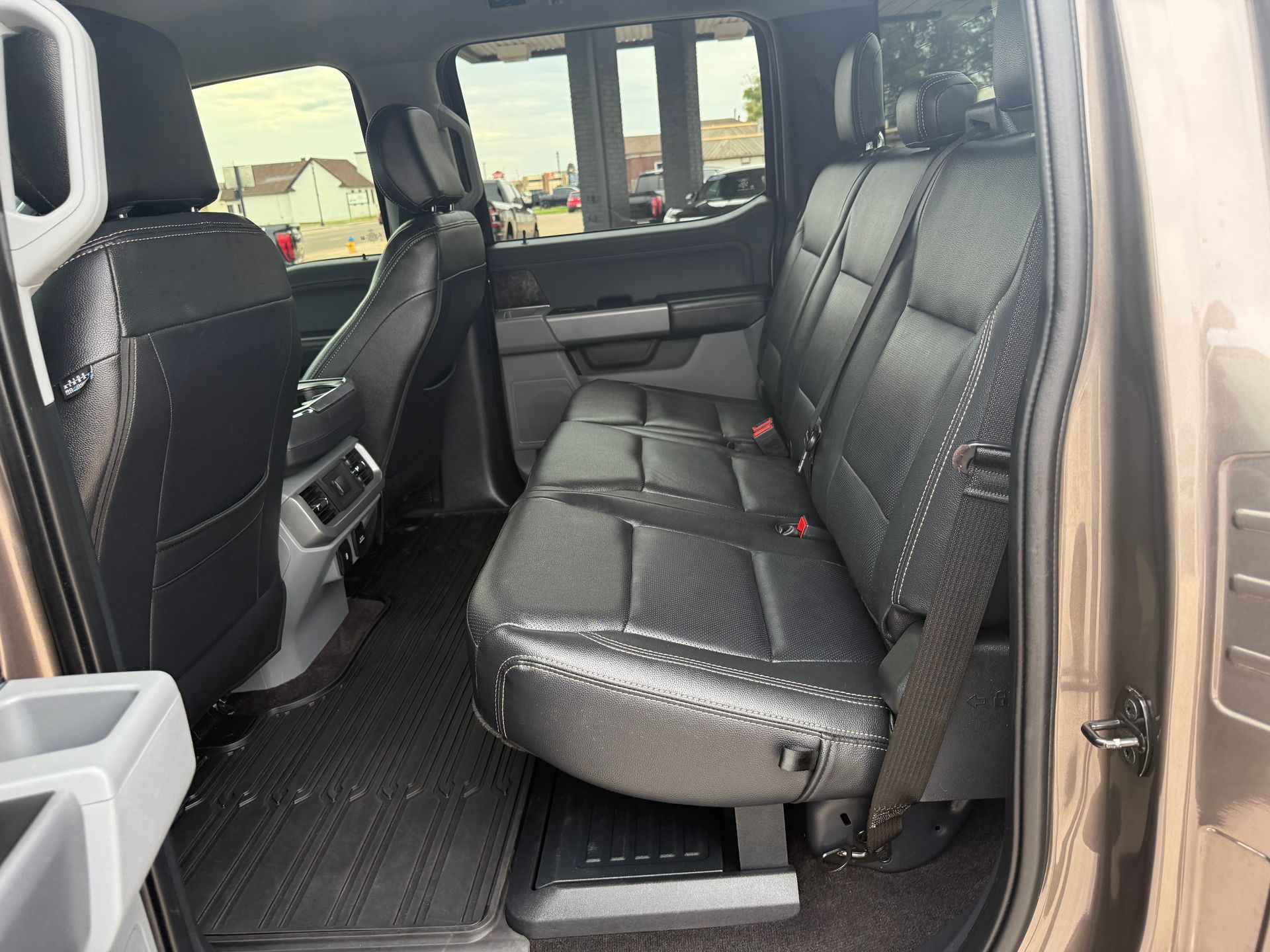 Interior view of a truck's back seats. Black leather seats, black floor mats, and beige door panels.